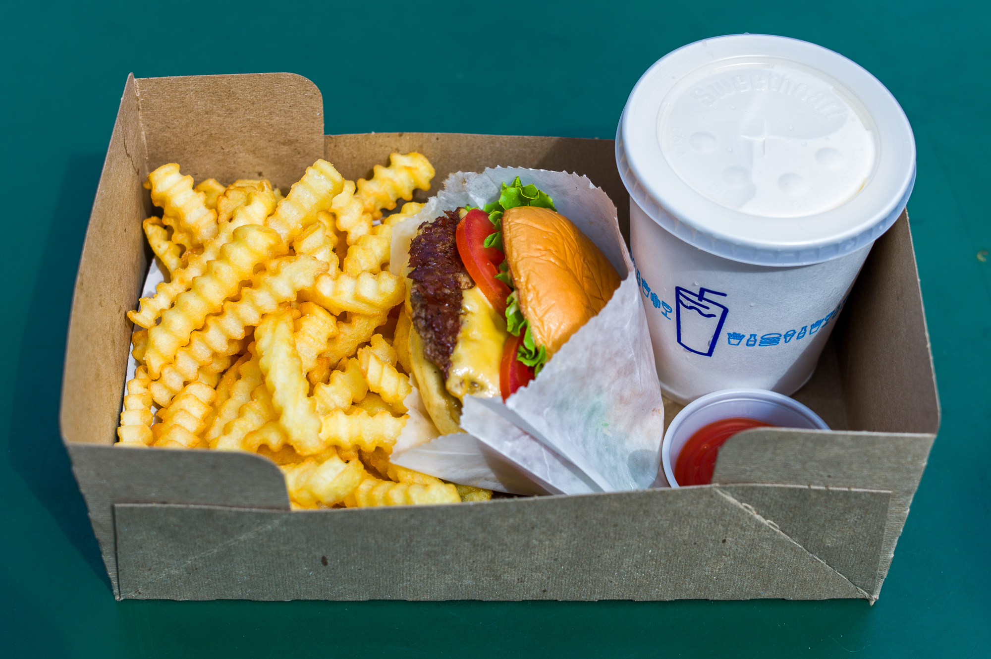 A Shake Shack burger, crinkle fries, and a drink in a paper box