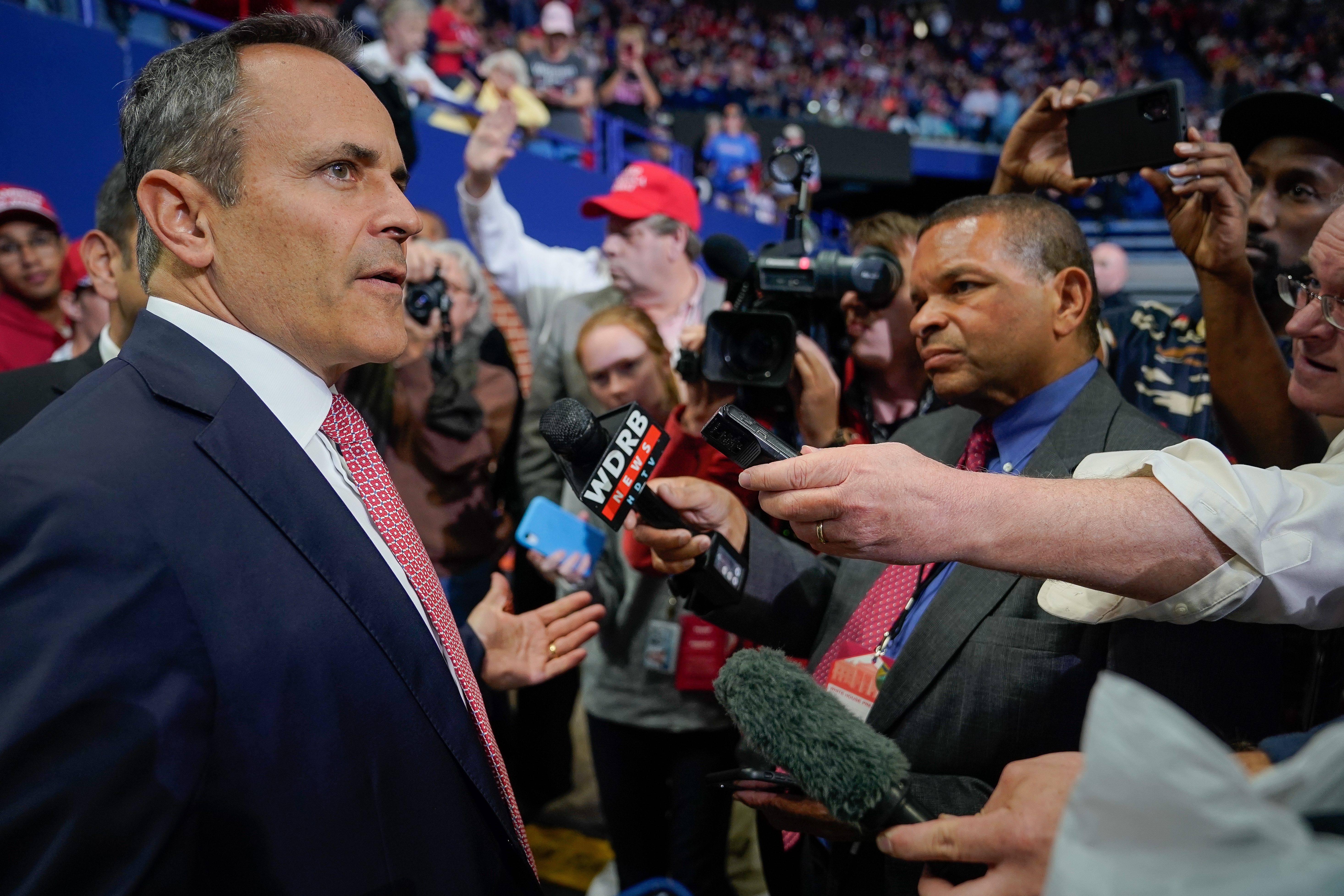 Matt Bevin speaks into a microphone held by a reporter at a crowded rally.