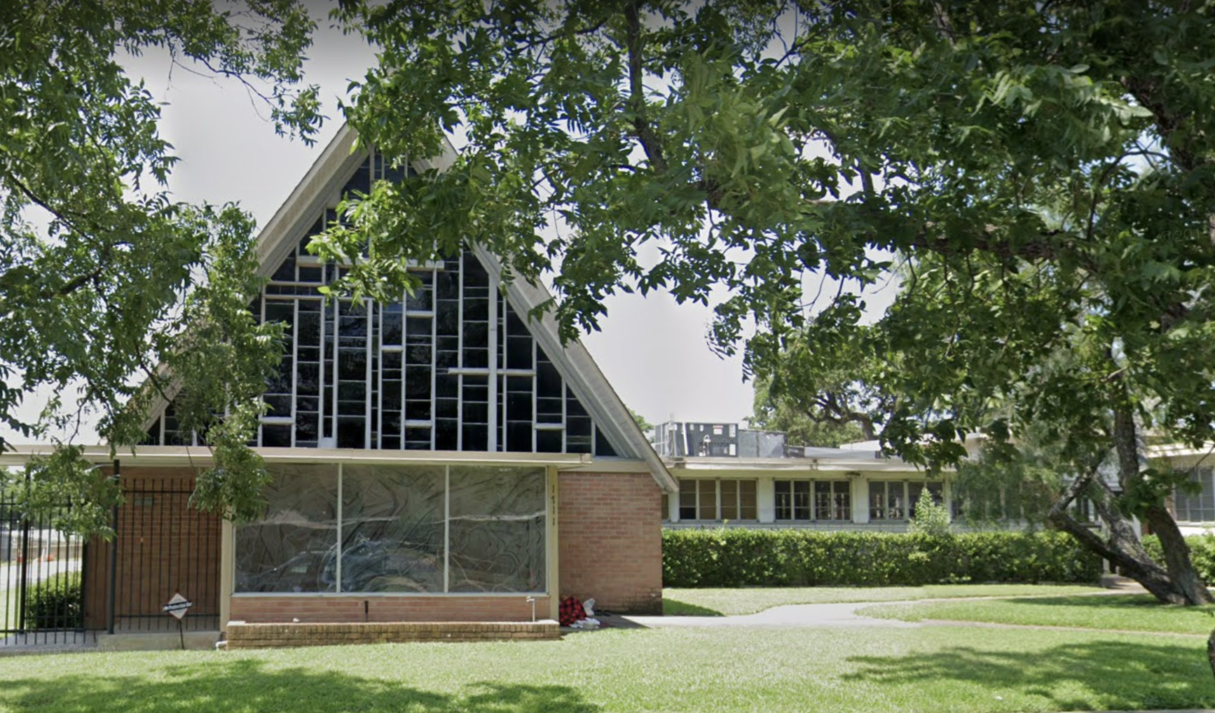 A photo of the exterior of an A-frame church with brick siding on the bottom and a grid of staggered rectangular windows filling the top of the frame. 