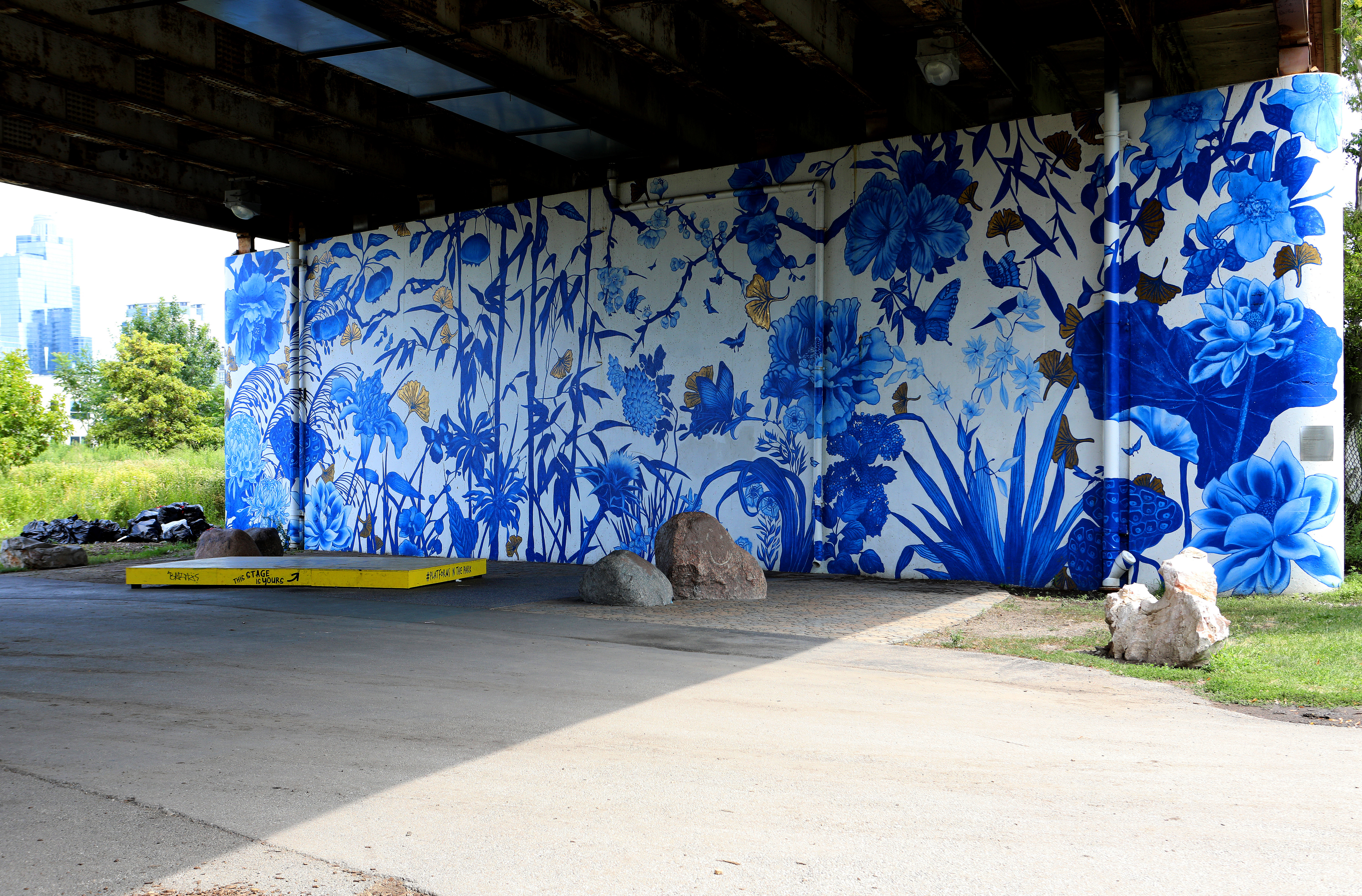 A blue and white floral mural on the wall of an underpass in a park. 