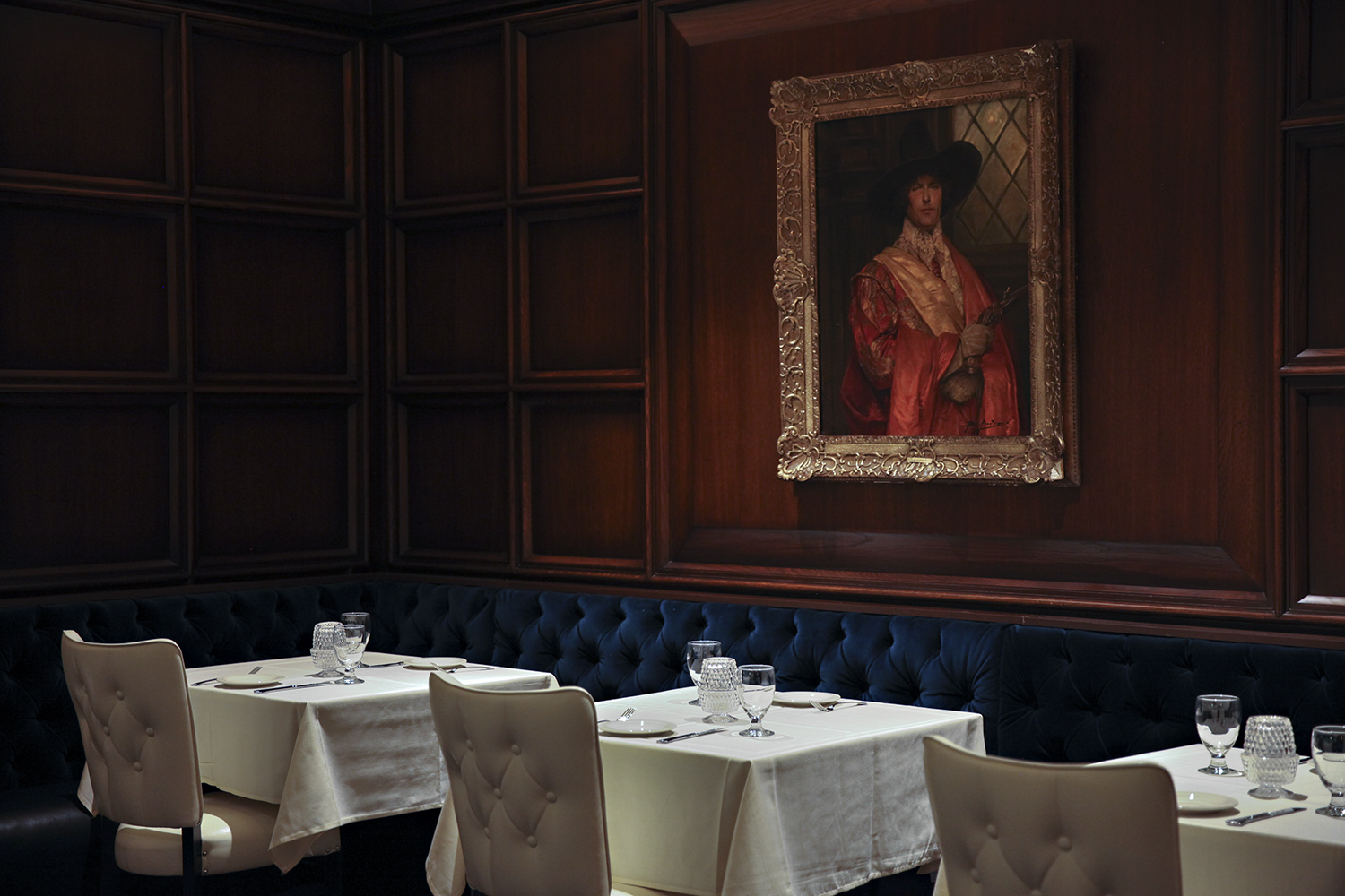 A line of white tablecloth tables in front of an oil painting of a regal looking guy
