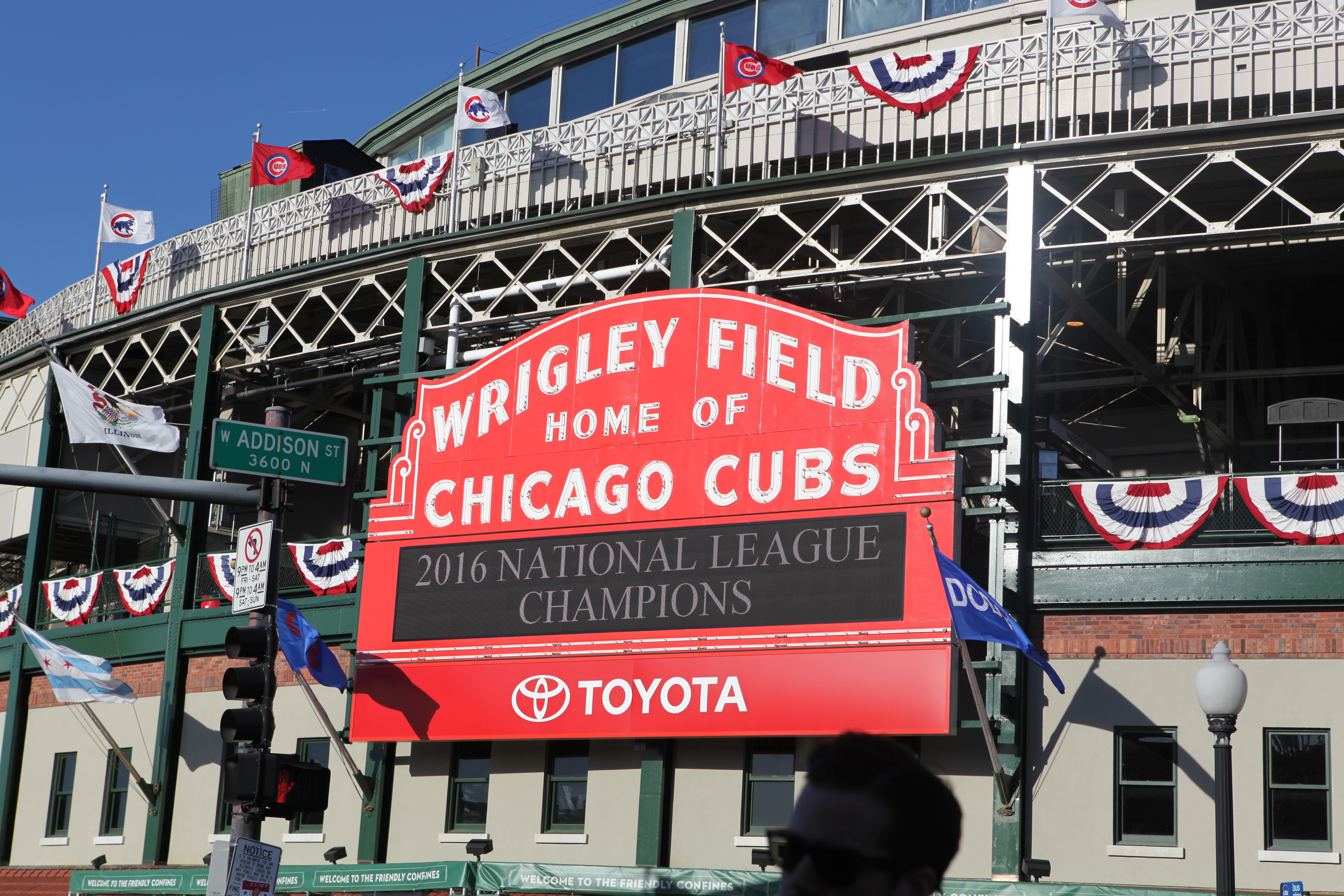 A red sign above the baseball field’s entrance reads: Wrigley Field Home of the Chicago Cubs.