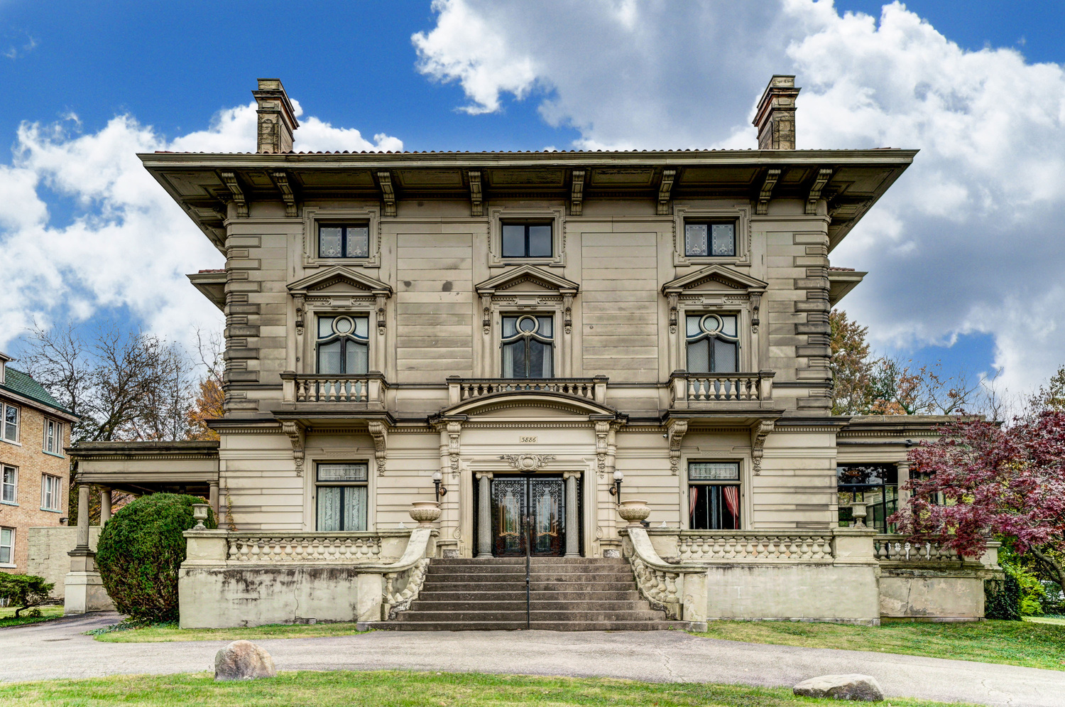 A three-story mansion made from stone sits with a stately set of stairs leading to the front door. 