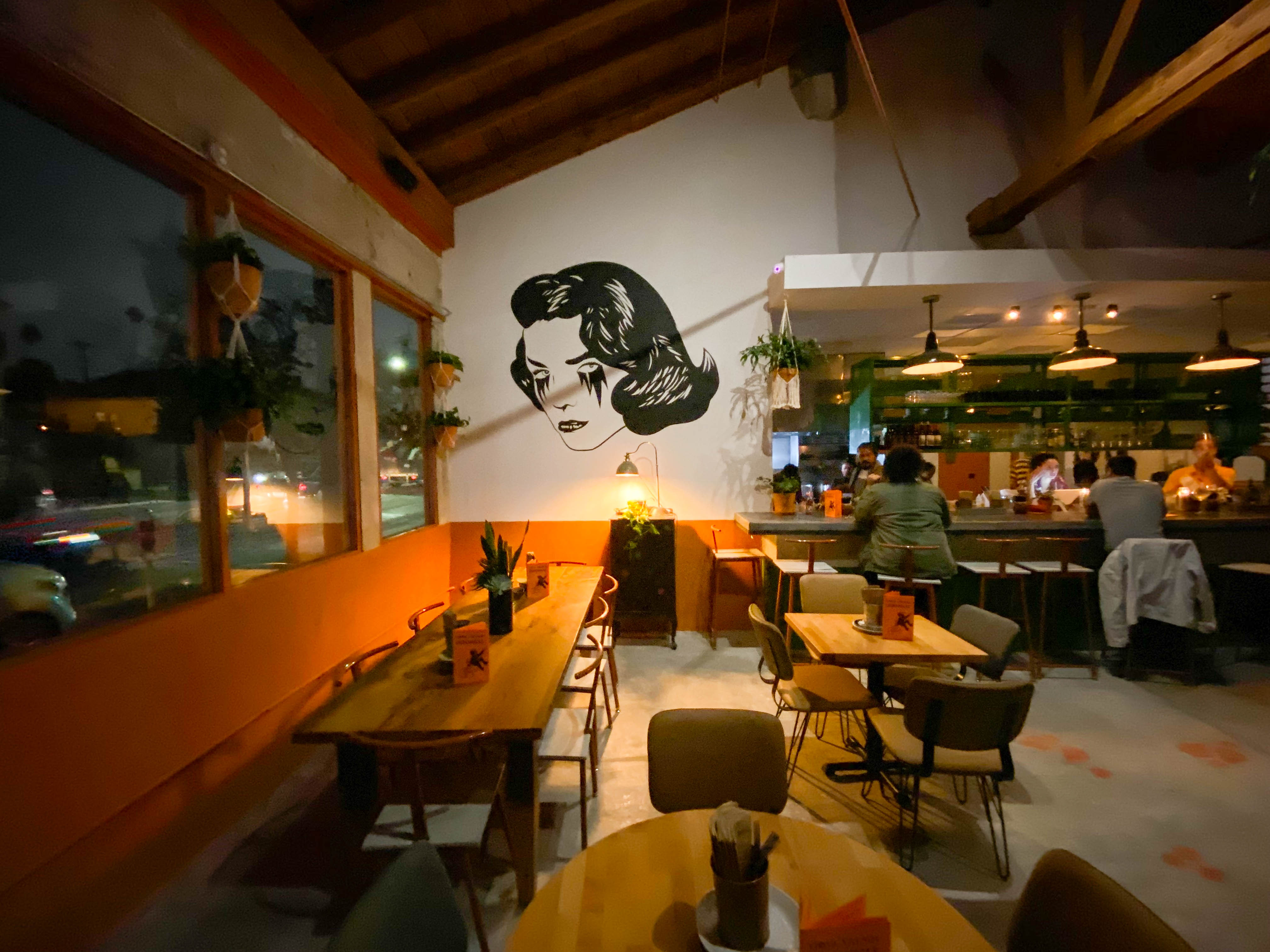 A dinnertime restaurant with mood lighting highlights a mural of a crying woman.