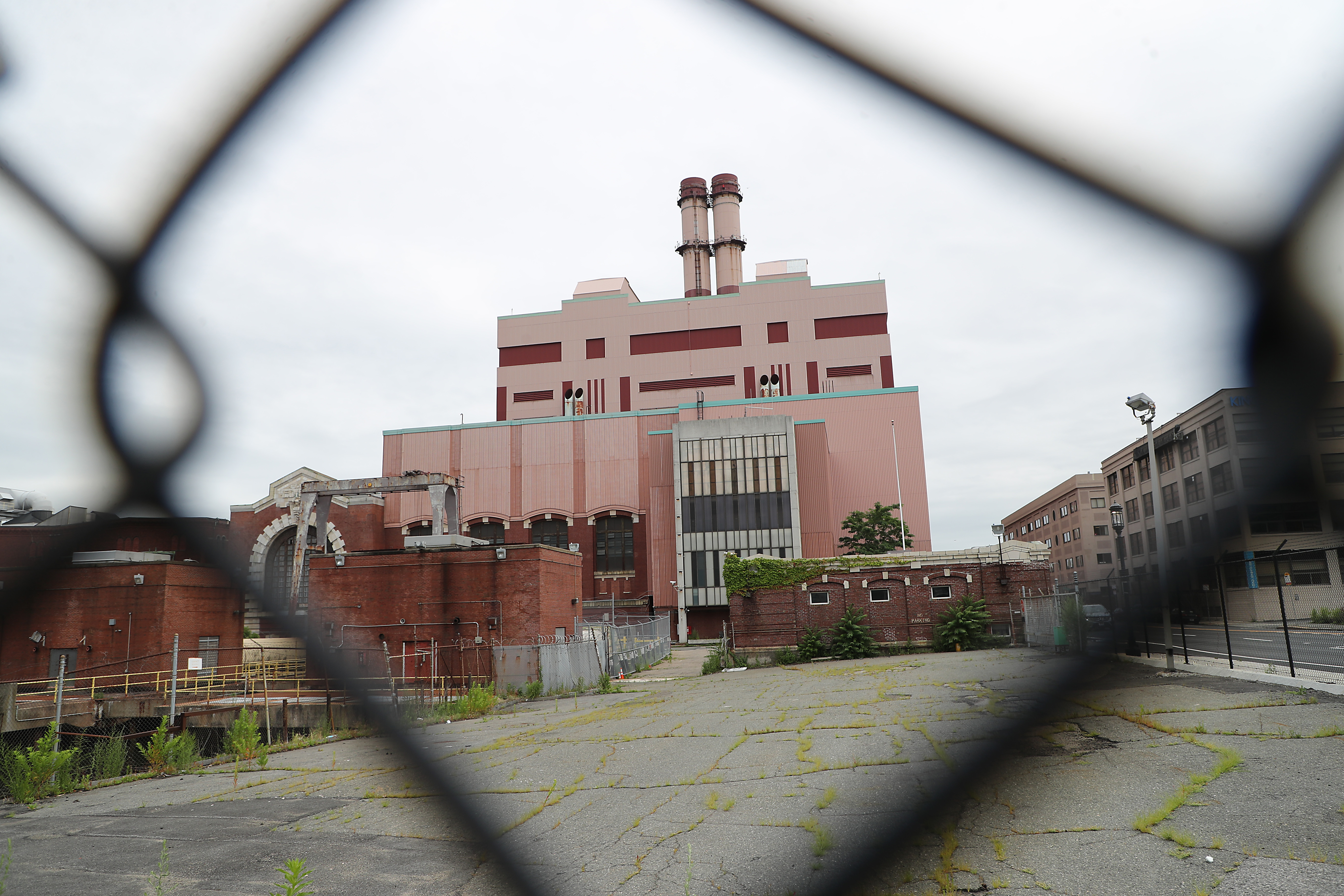 A large, box, shuttered power plant as seen through a chain-link fence. 