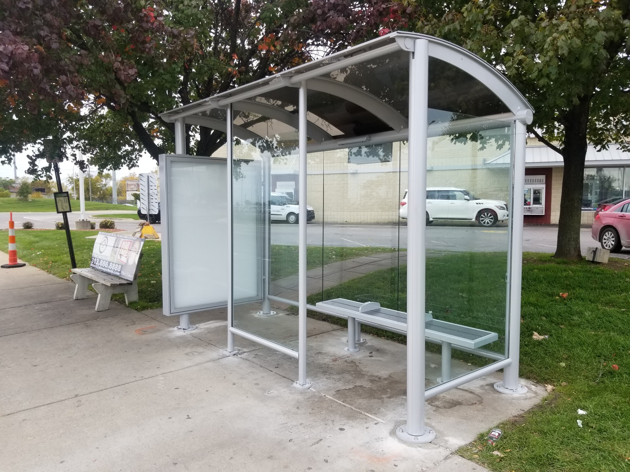 A metal bus shelter with a narrow bench and curved roof. There’s a solar panel on top.
