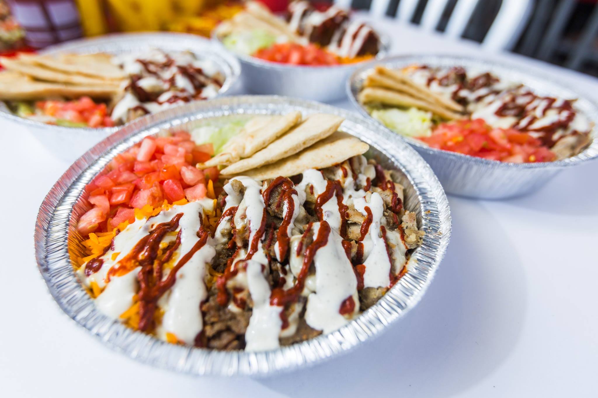 A foil bowl full of gyros and drizzle with white and red sauces.