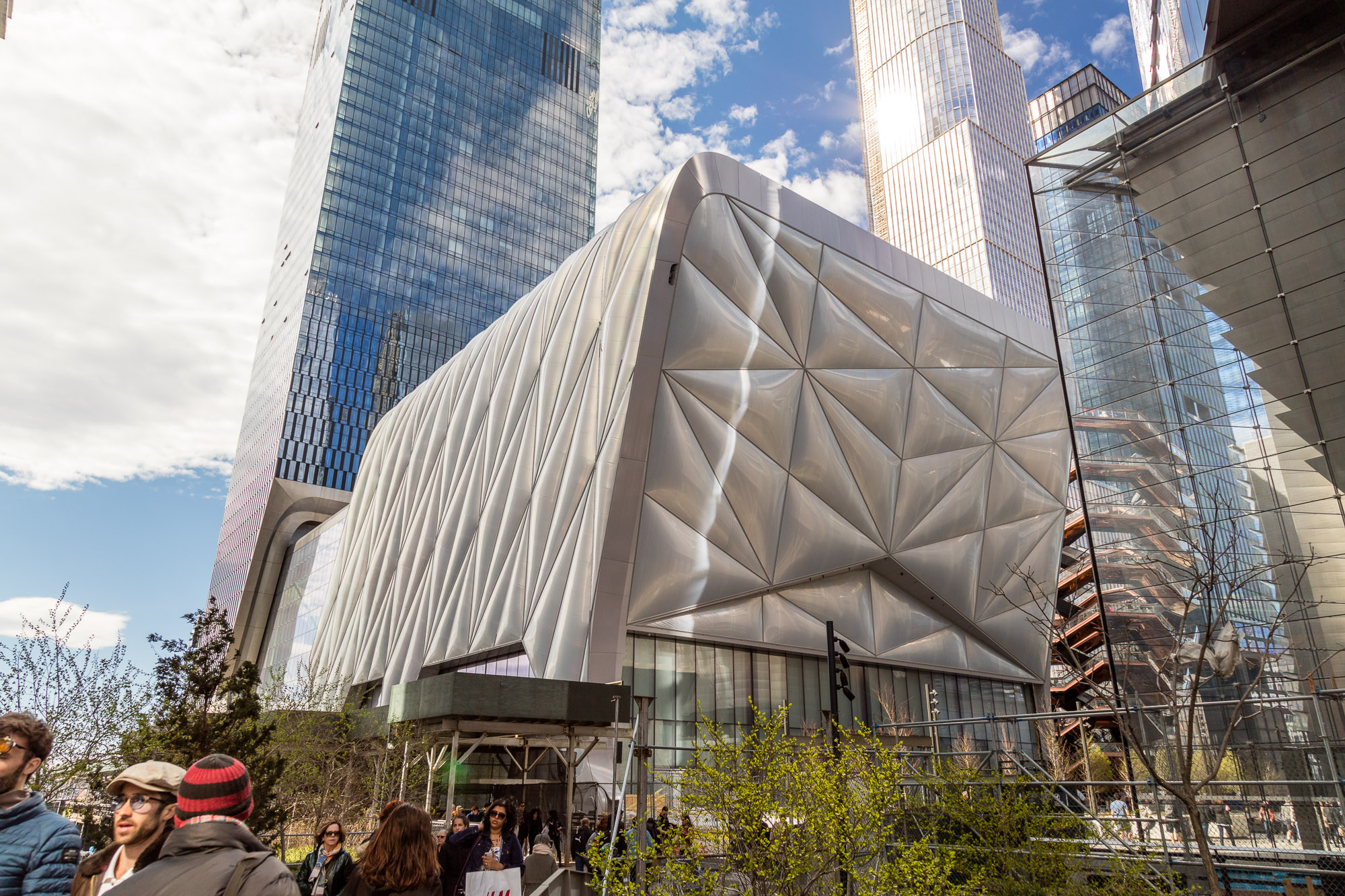 A square-like structure with a silver facade, surrounded by skyscrapers.