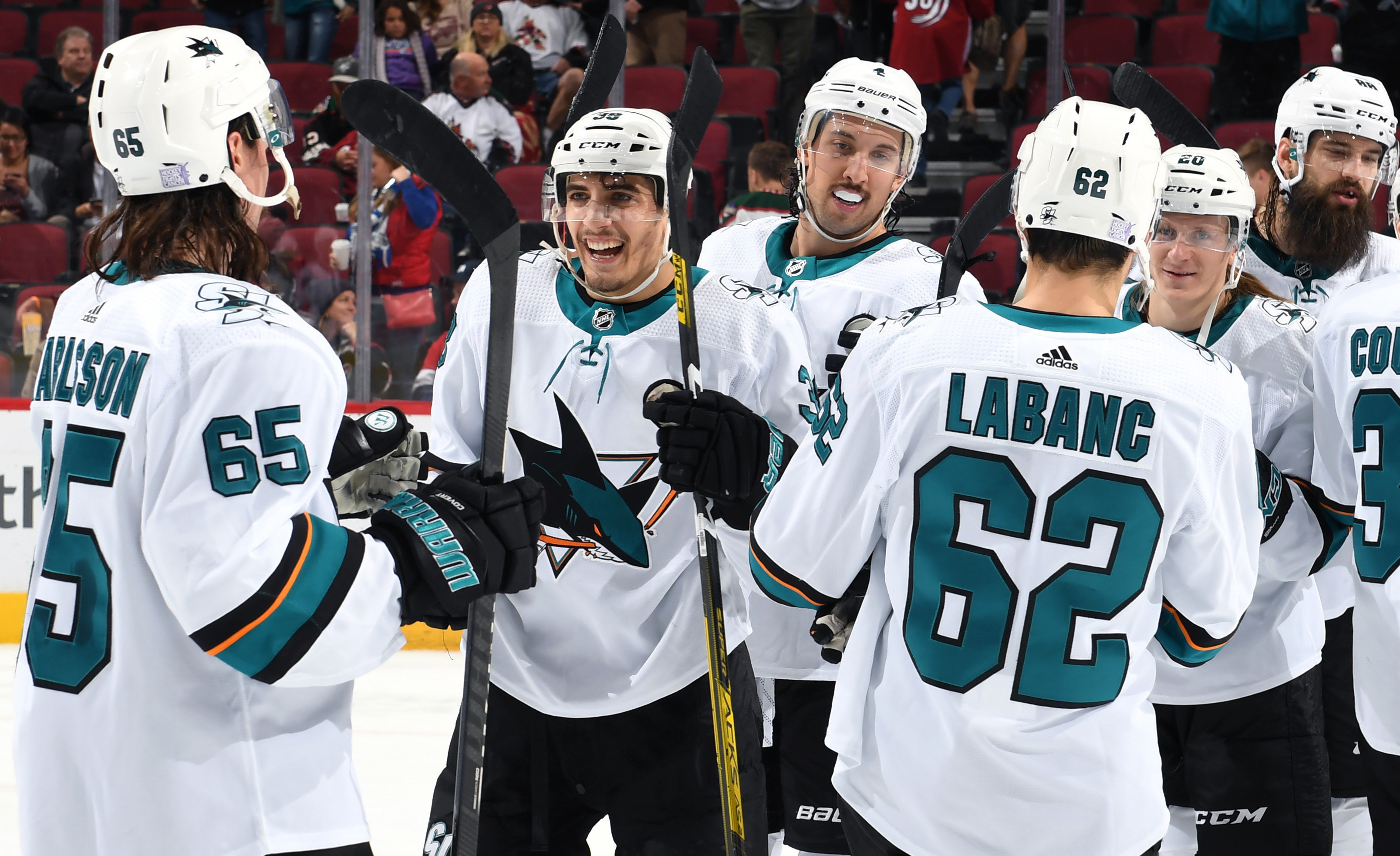 Mario Ferraro #38 of the San Jose Sharks is congratulated by Erik Karlsson #65, Kevin LaBanc #62 and teammates following a 4-2 victory against the Arizona Coyotes during the NHL game at Gila River Arena on November 30, 2019 in Glendale, Arizona.