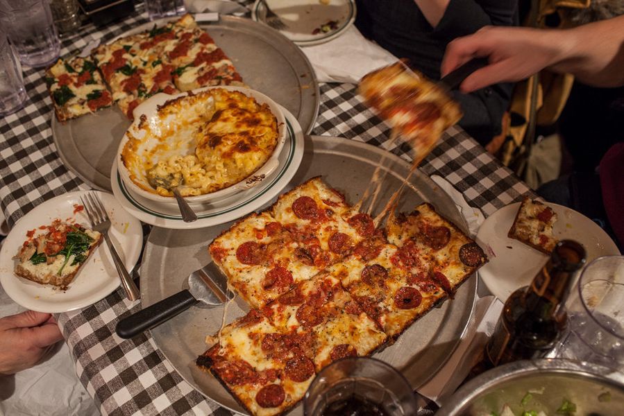 a square pepperoni pizza being served onto plates over a black and white checked tablecloth with macaroni and cheese in a dish.