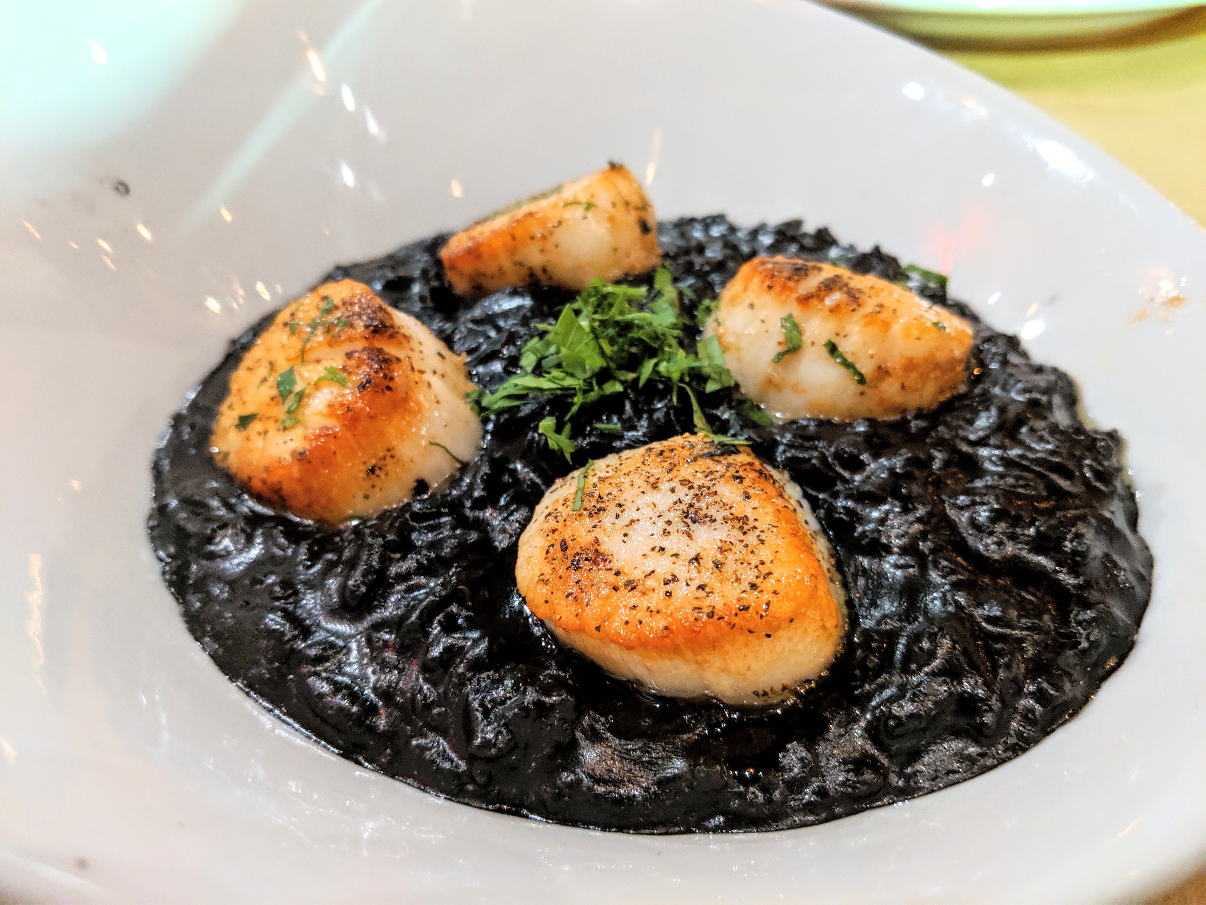 Four pan-seared scallops sit on a bed of black squid ink risotto in a white bowl