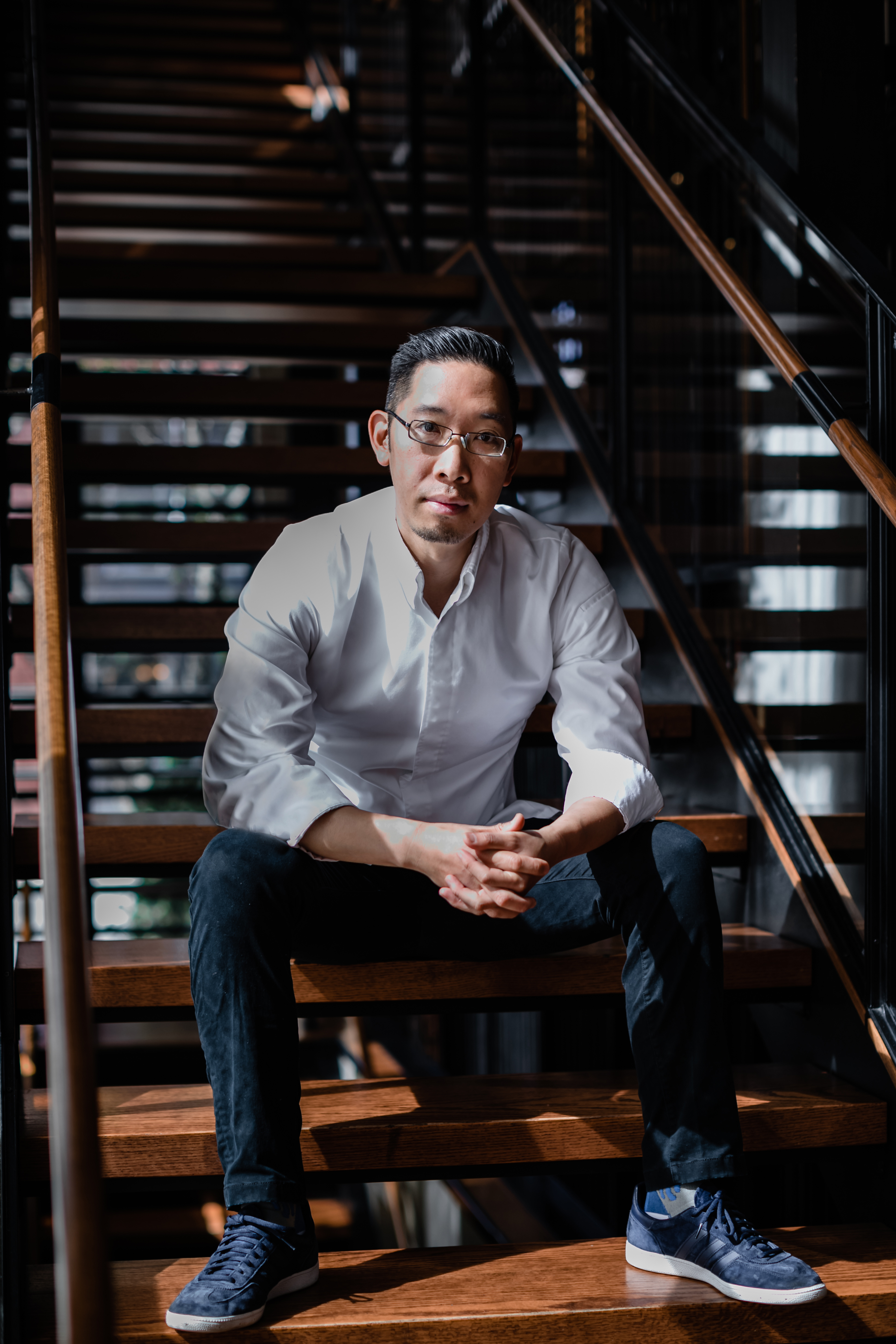 A portrait shot of an Asian-American chef in a white coat sitting on a flight of stairs.