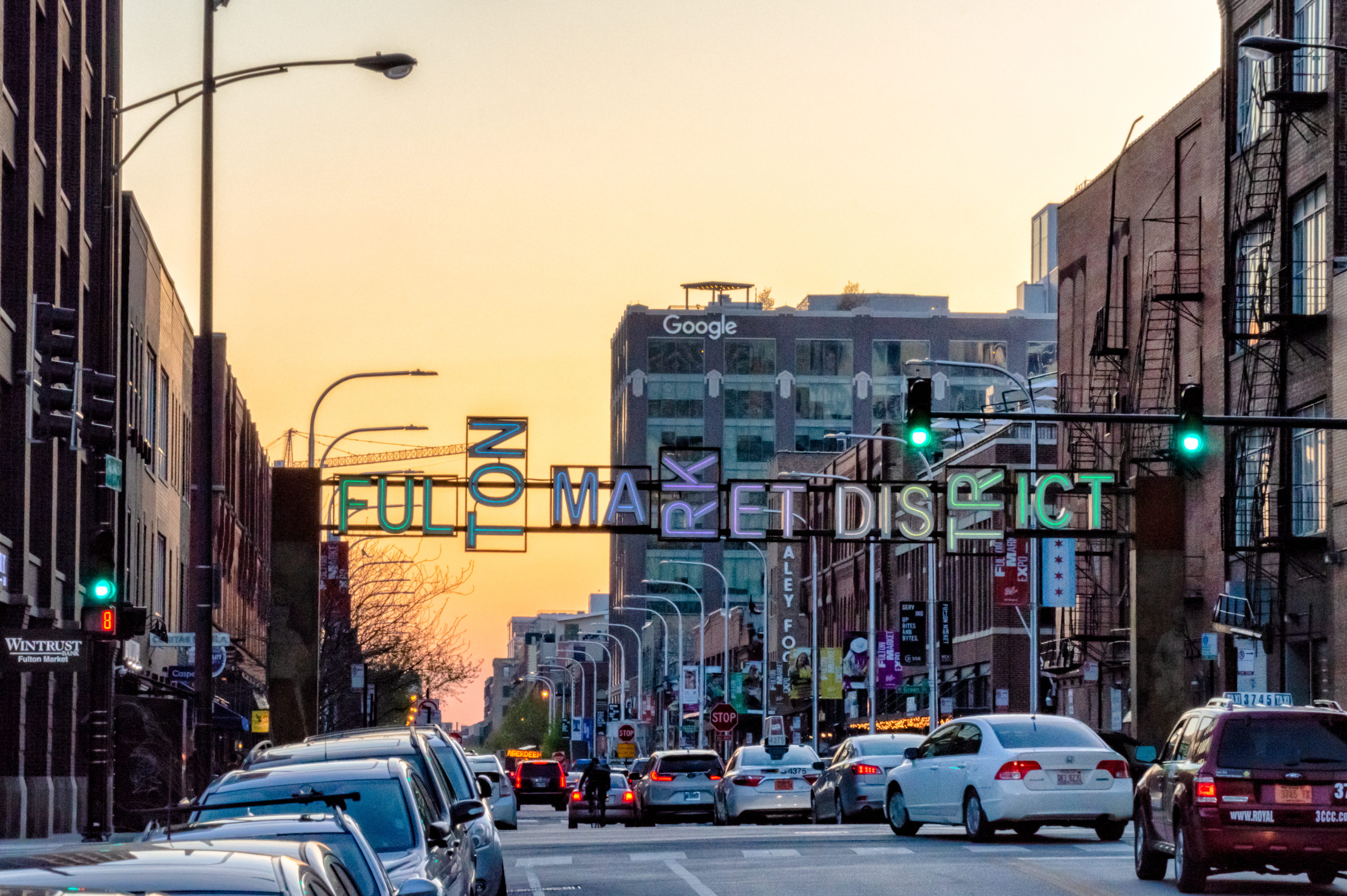 An image of Fulton Market Street with a neon gateway sign at sunset.
