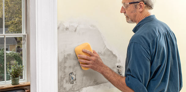 Person uses a damp sponge to smooth the final coat on a plaster patch.