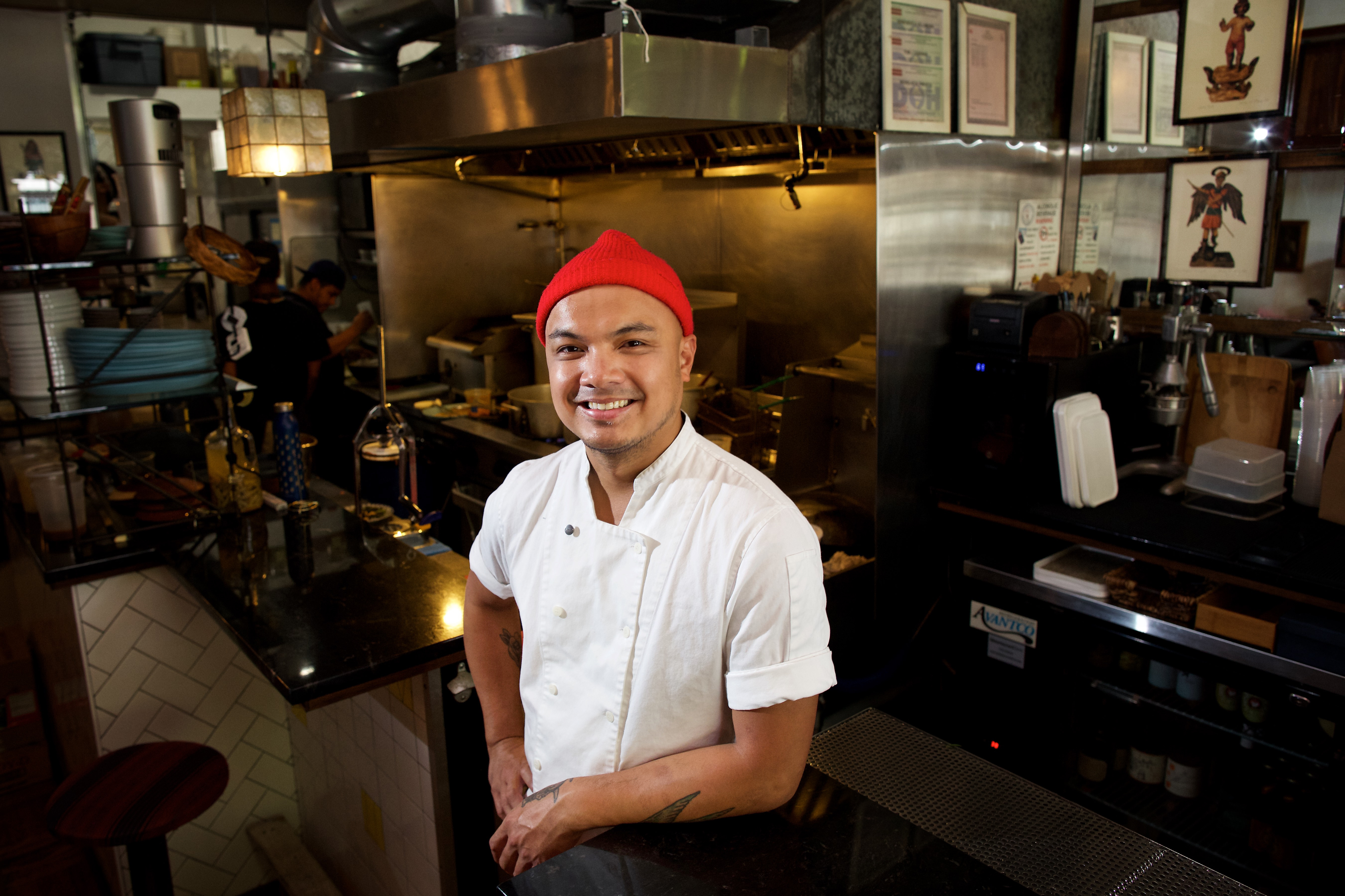 A picture of Tom Cunanan of Bad Saint standing in his restaurant with a red beanie on