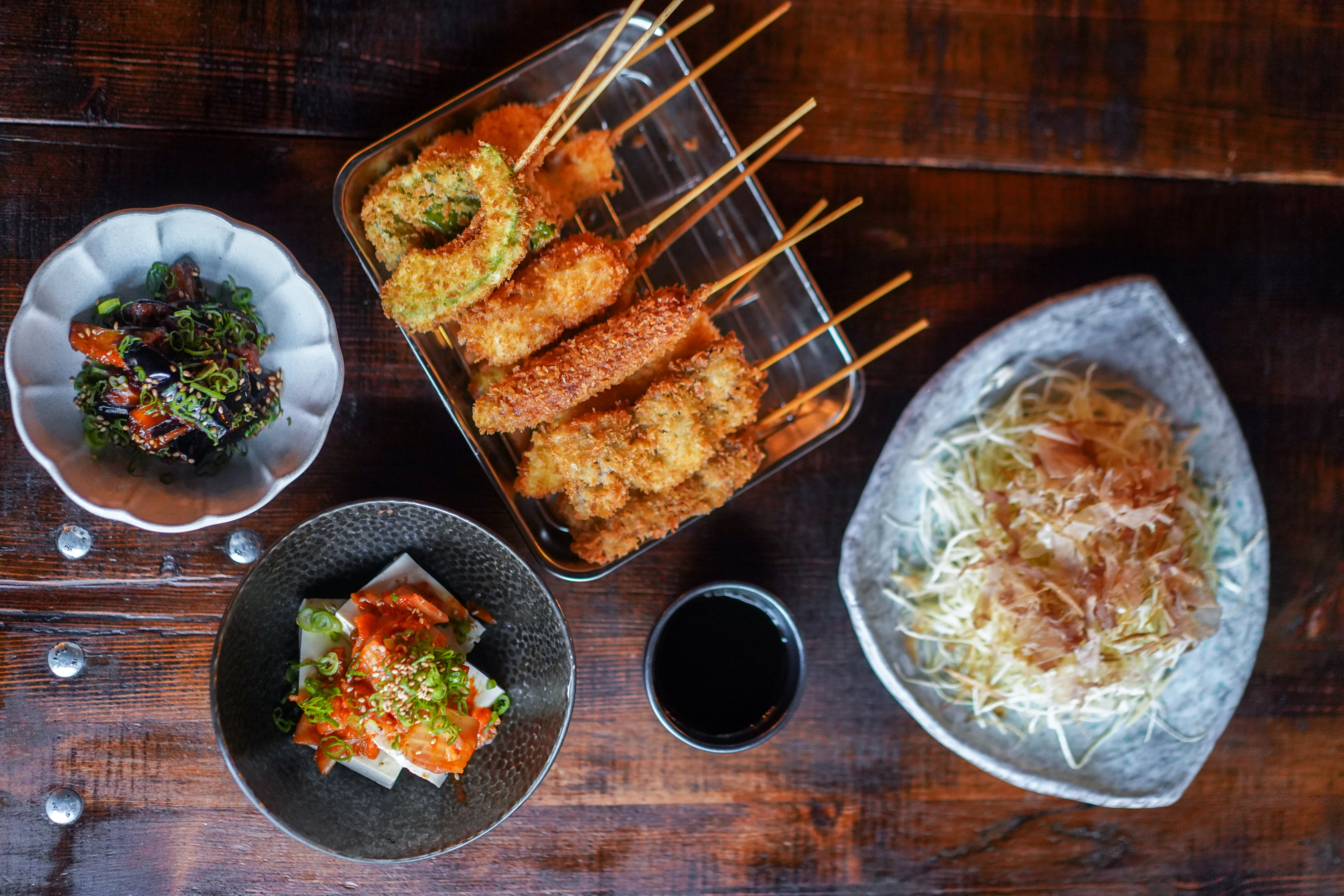 A top-down view of various Japanese deep-fried skewers and rice dishes from Taku.