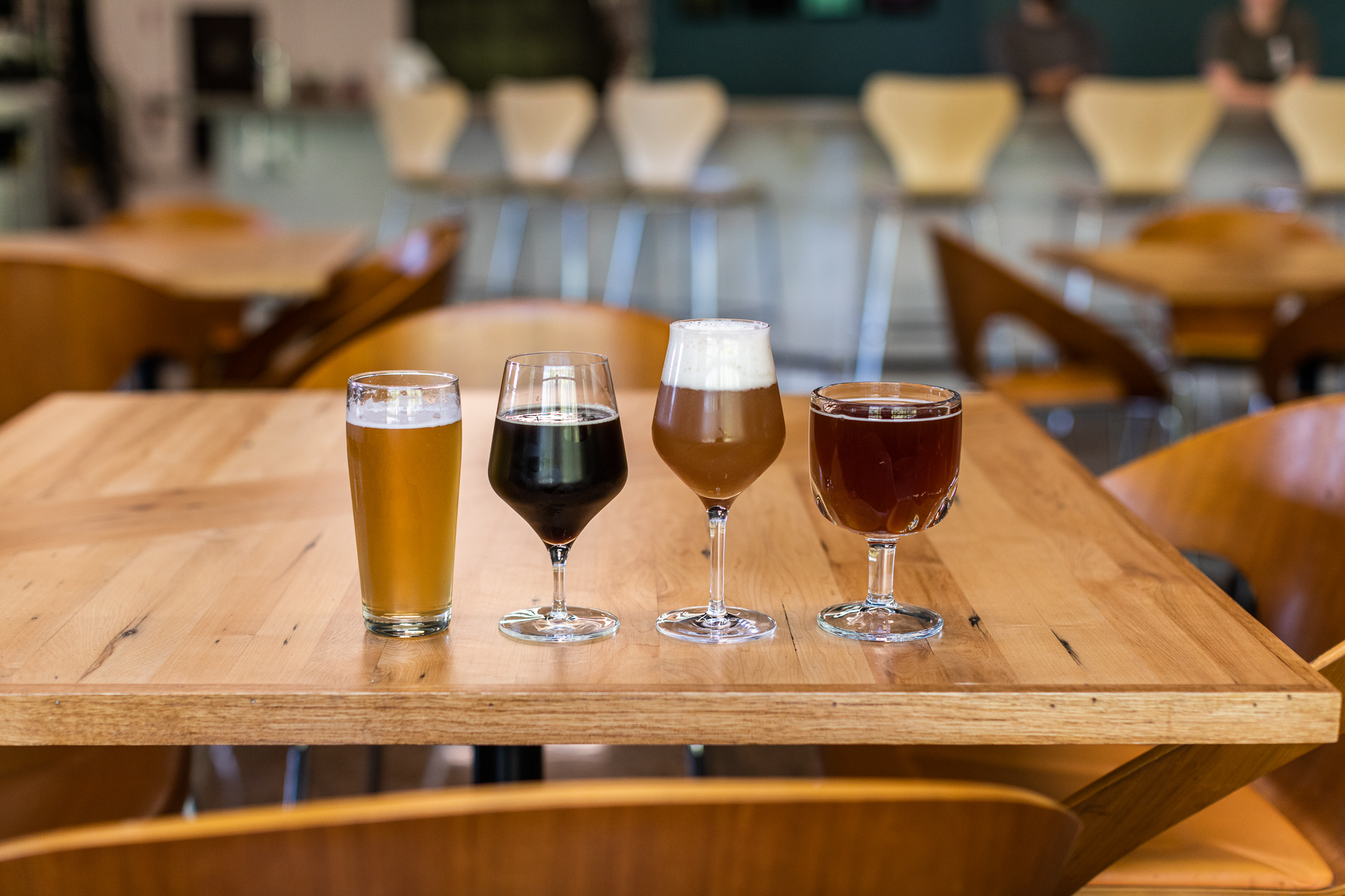 Four glasses of different colored beer in a row on a wooden table.