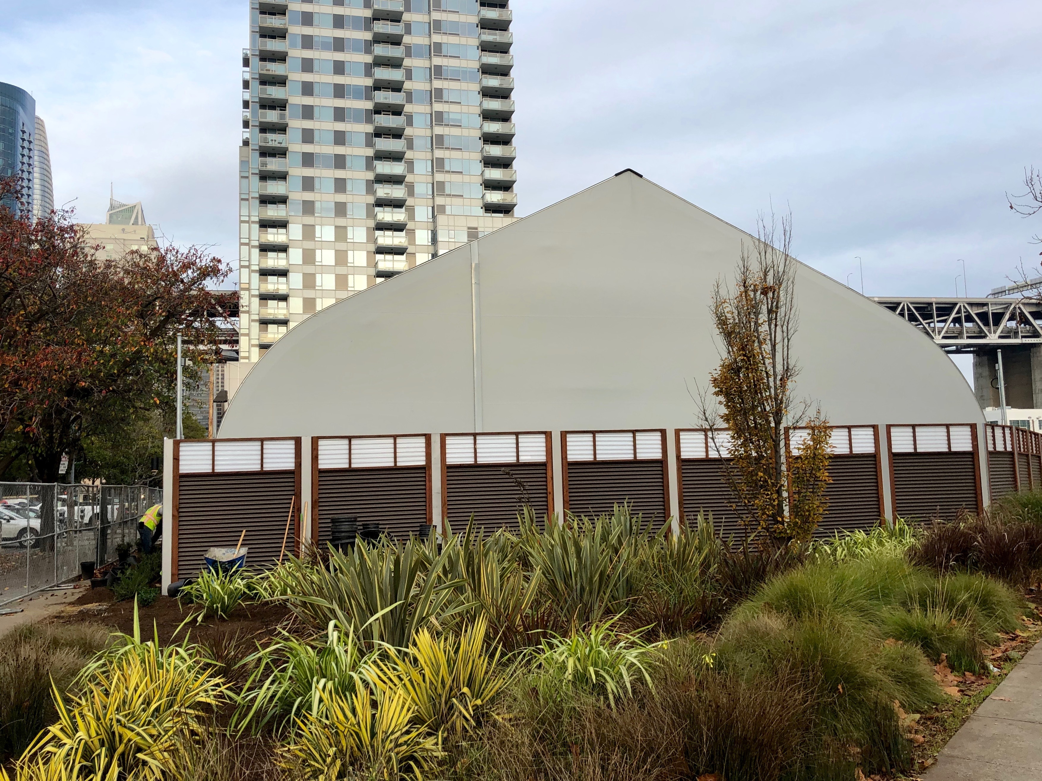 A tent-like white structure, with tall glass-covered high-rises in the background.