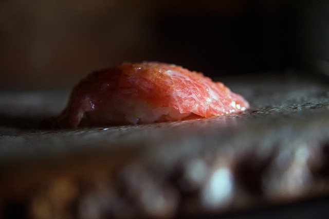 A slice of pink fatty tuna, marbled with fat, sits over a small mound of rice.