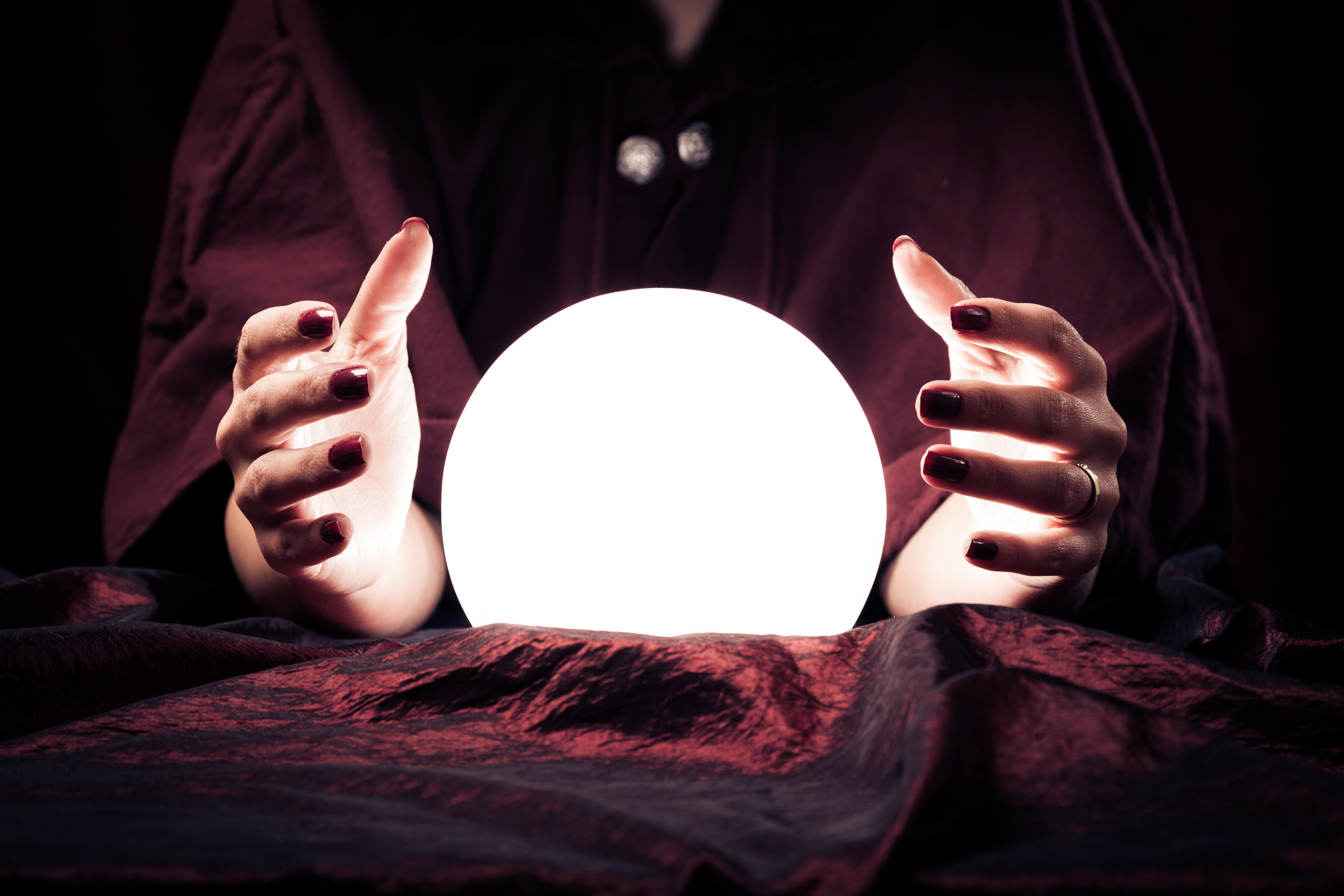 Manicured fortune teller’s hands hover around a glowing crystal ball.