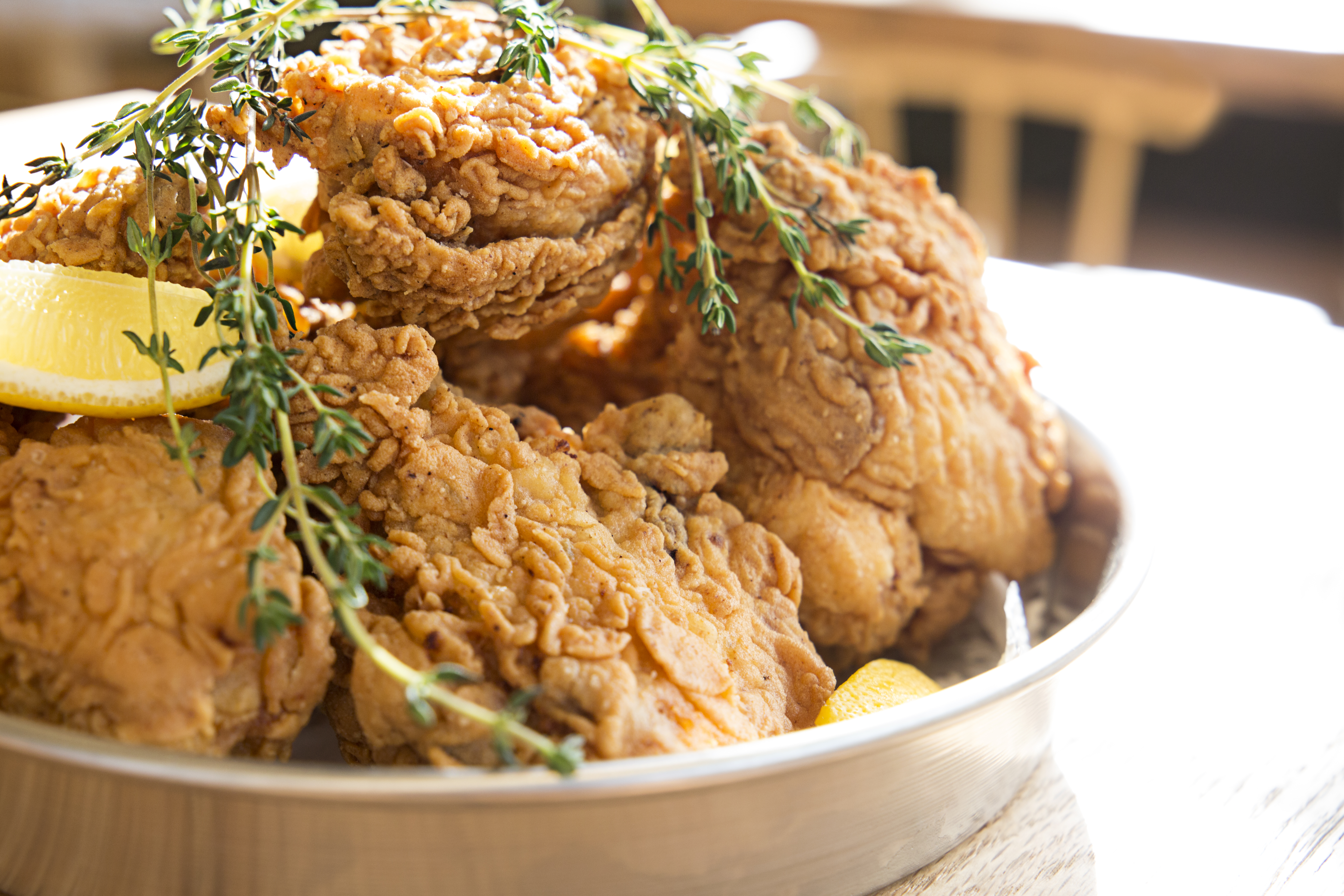 A plate of fried chicken from Southern Proper, a restaurant in Boston’s South End neighborhood. The chicken is adorned with sprigs of thyme and lemon wedges, and is served in a pie tin.