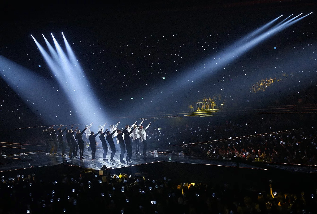 Dancers on a stage are lit by spotlights and surrounded by an arena of spectators.