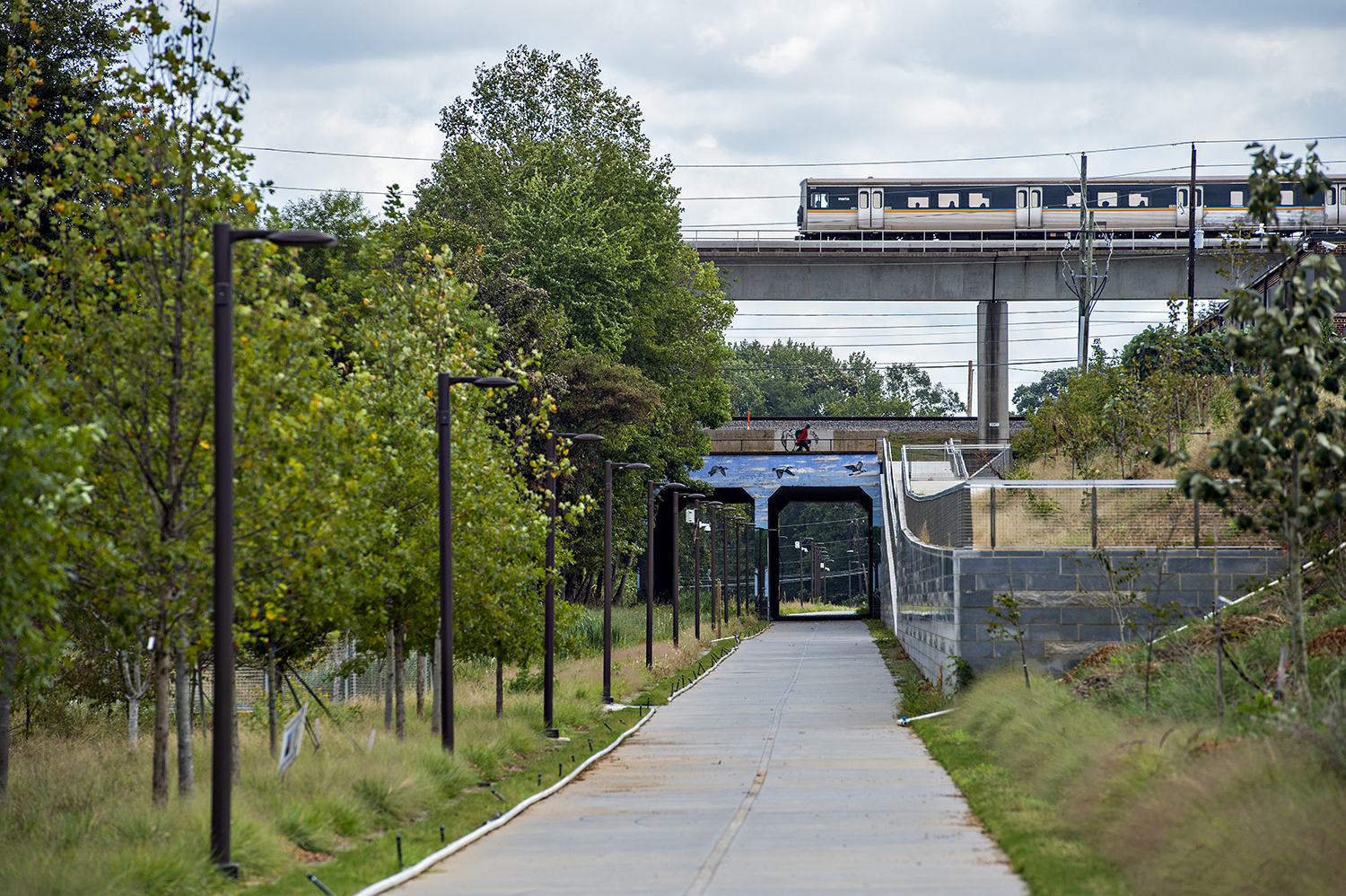 A concrete path with a MARTA train going over the top of it, with trees and light posts on either side.