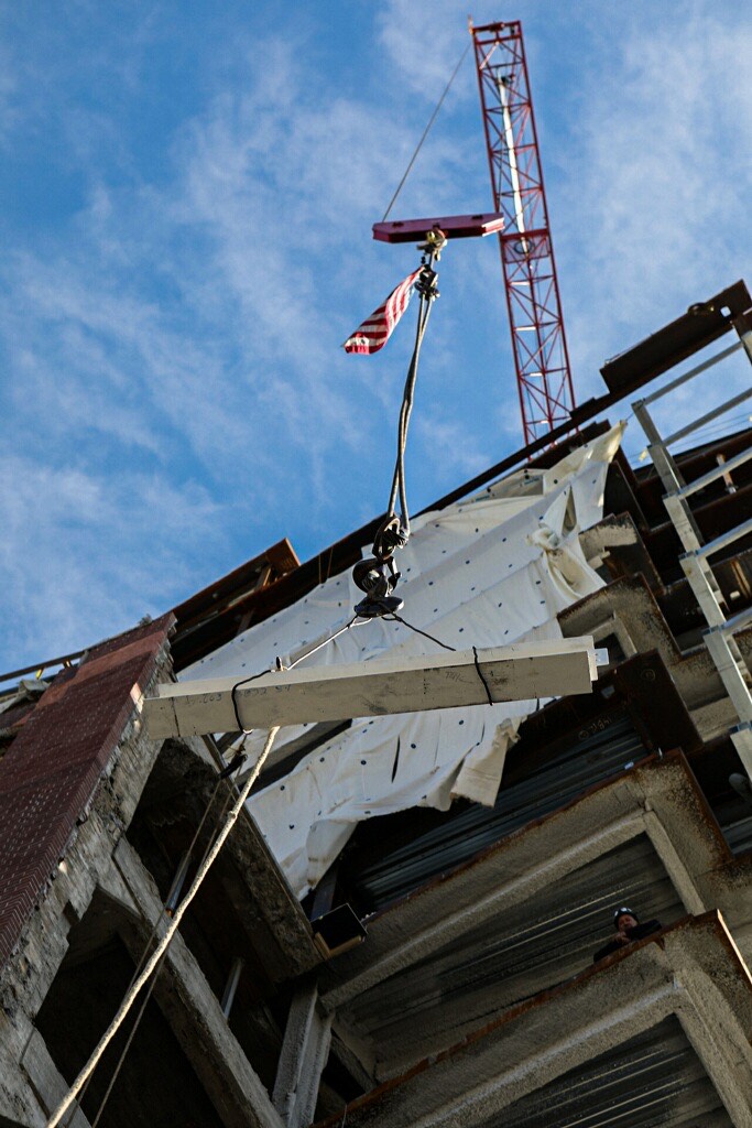 A crane with a flag putting a beam into place on a 13-story building.