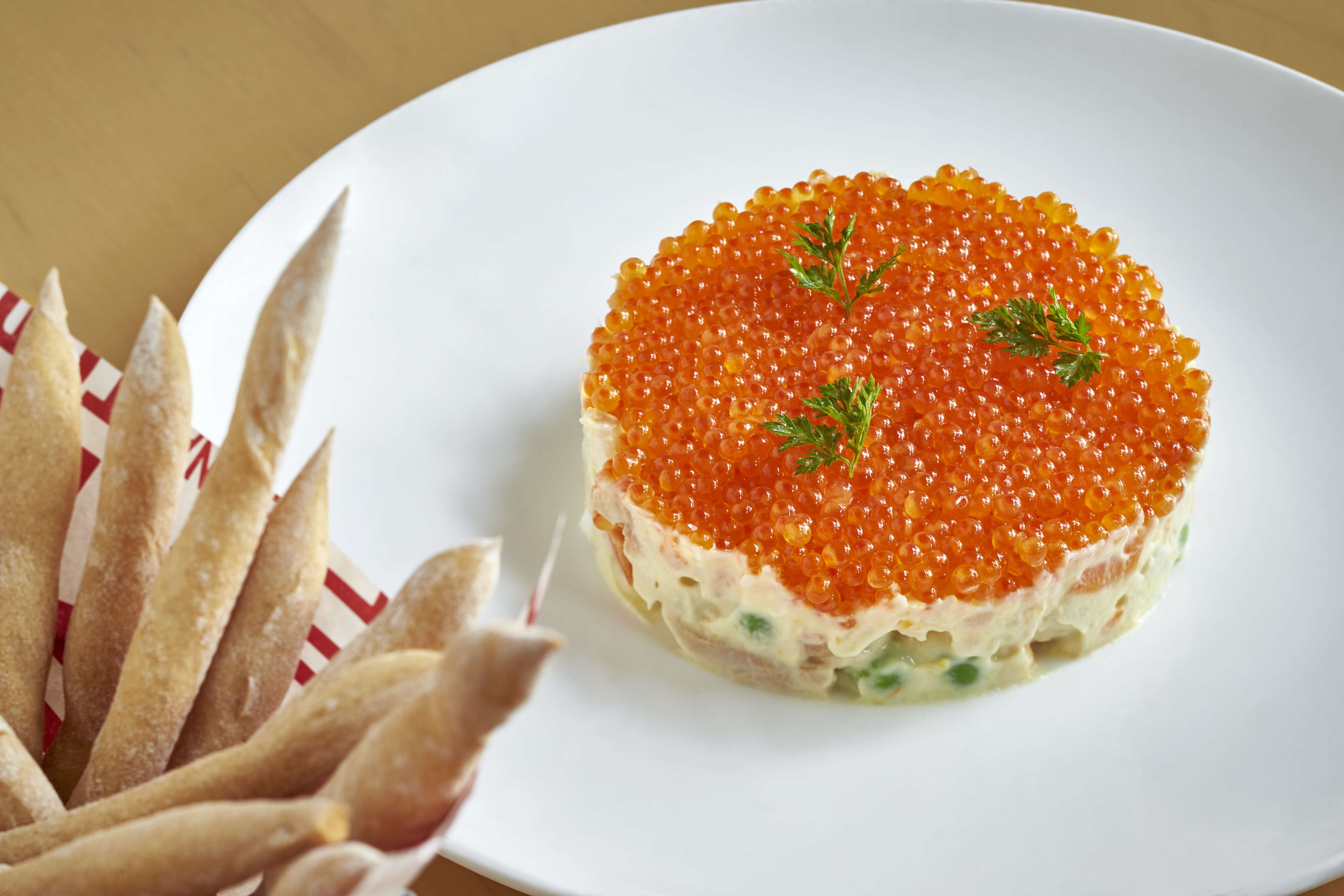A fancy disc of Spanish trout roe on white plate with a side of breadsticks.
