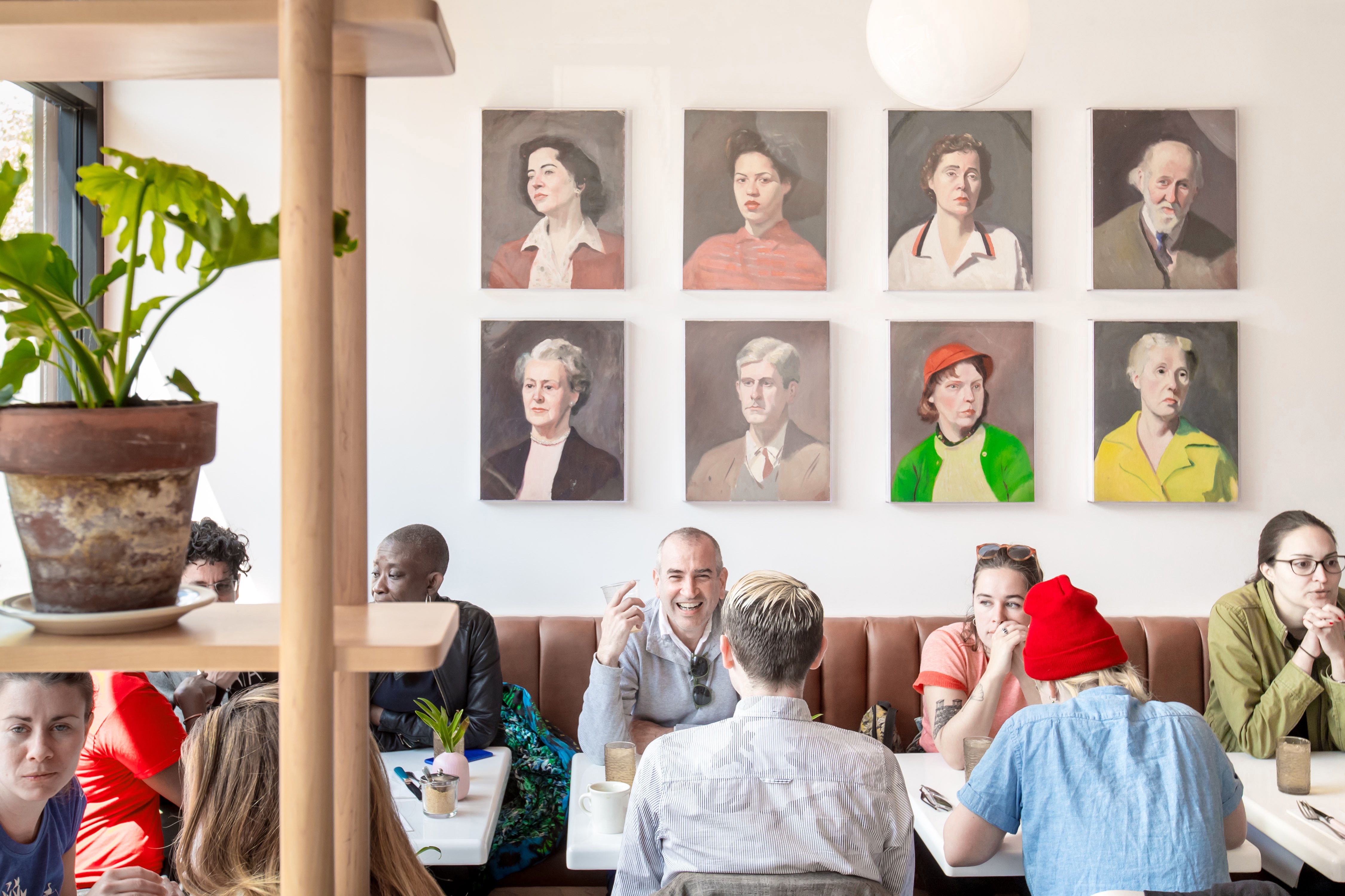 Diners sit in tables in a row with portraits hanging on a wall above them