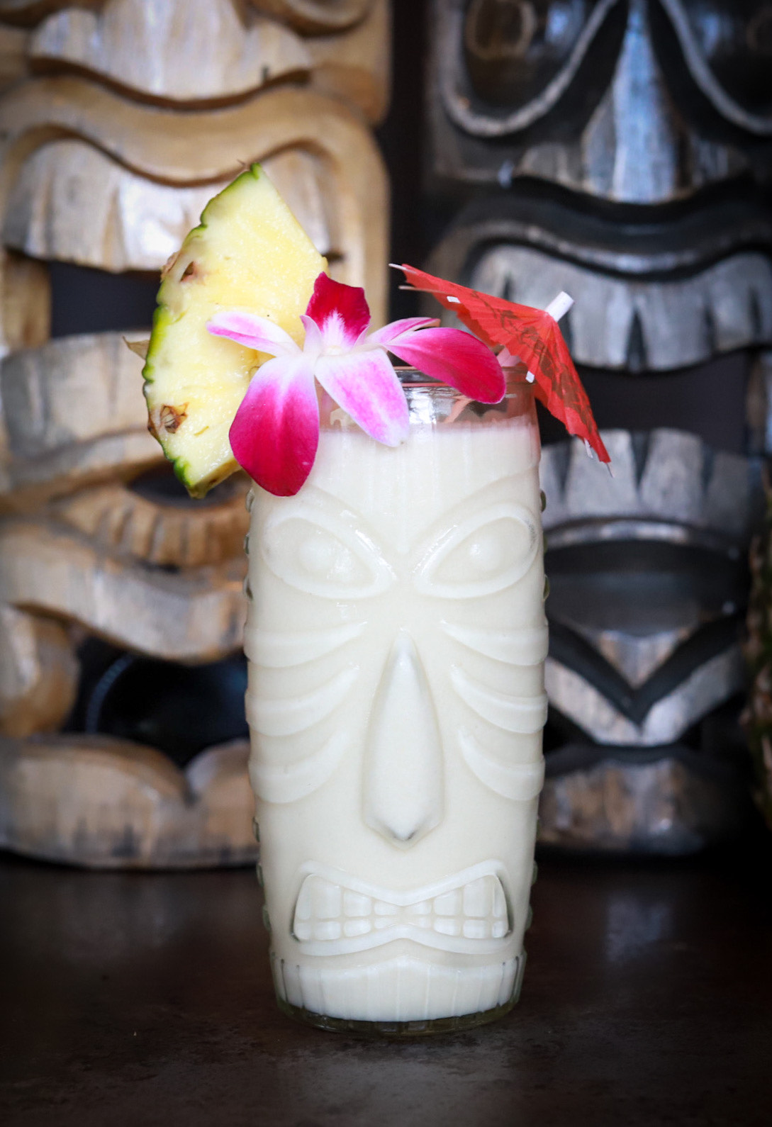 A pina colada decorated with orchids in a clear tiki mug. 