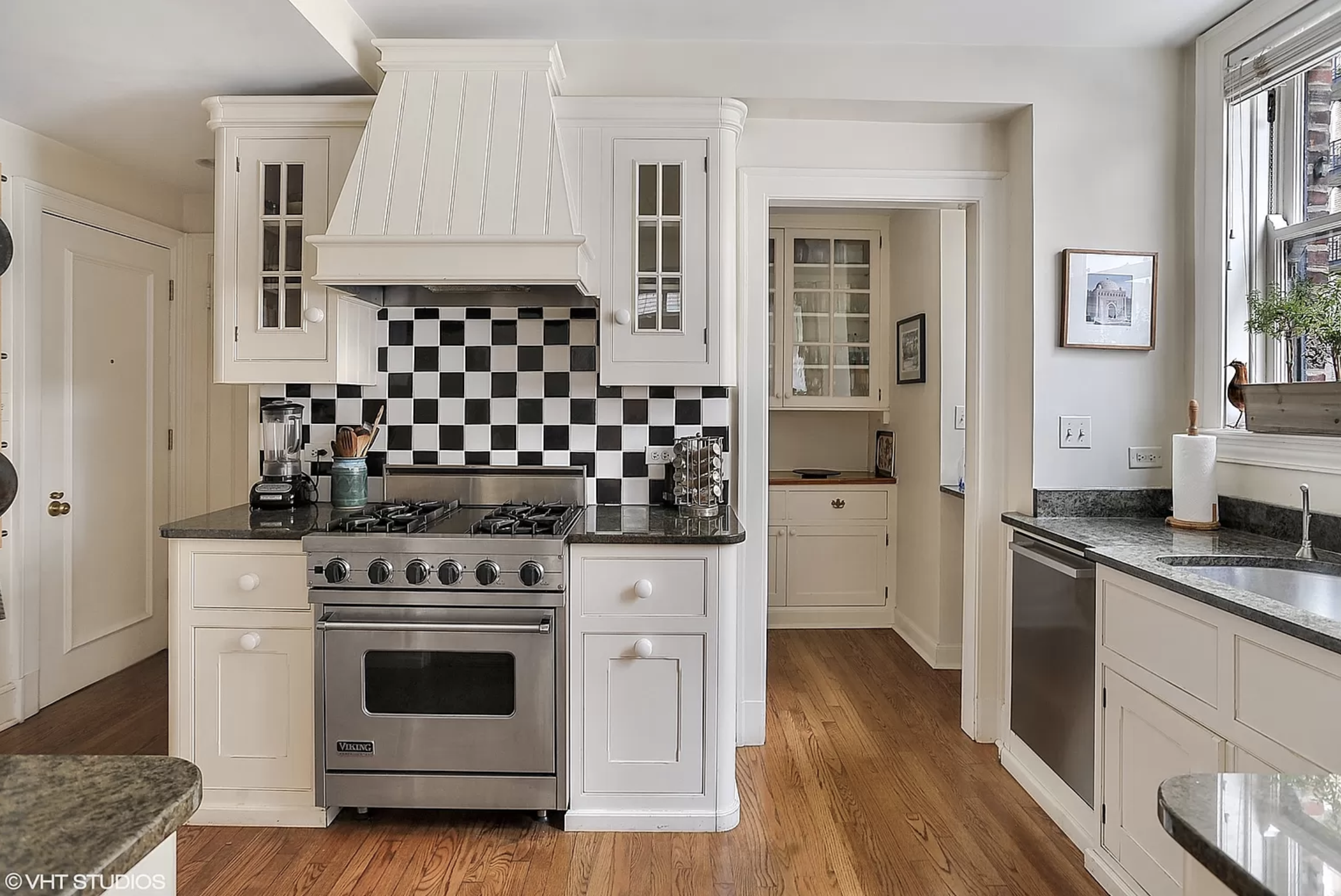 A kitchen with white cabinets, a checkered tile backsplash, a butler’s pantry, and a window over the sink.