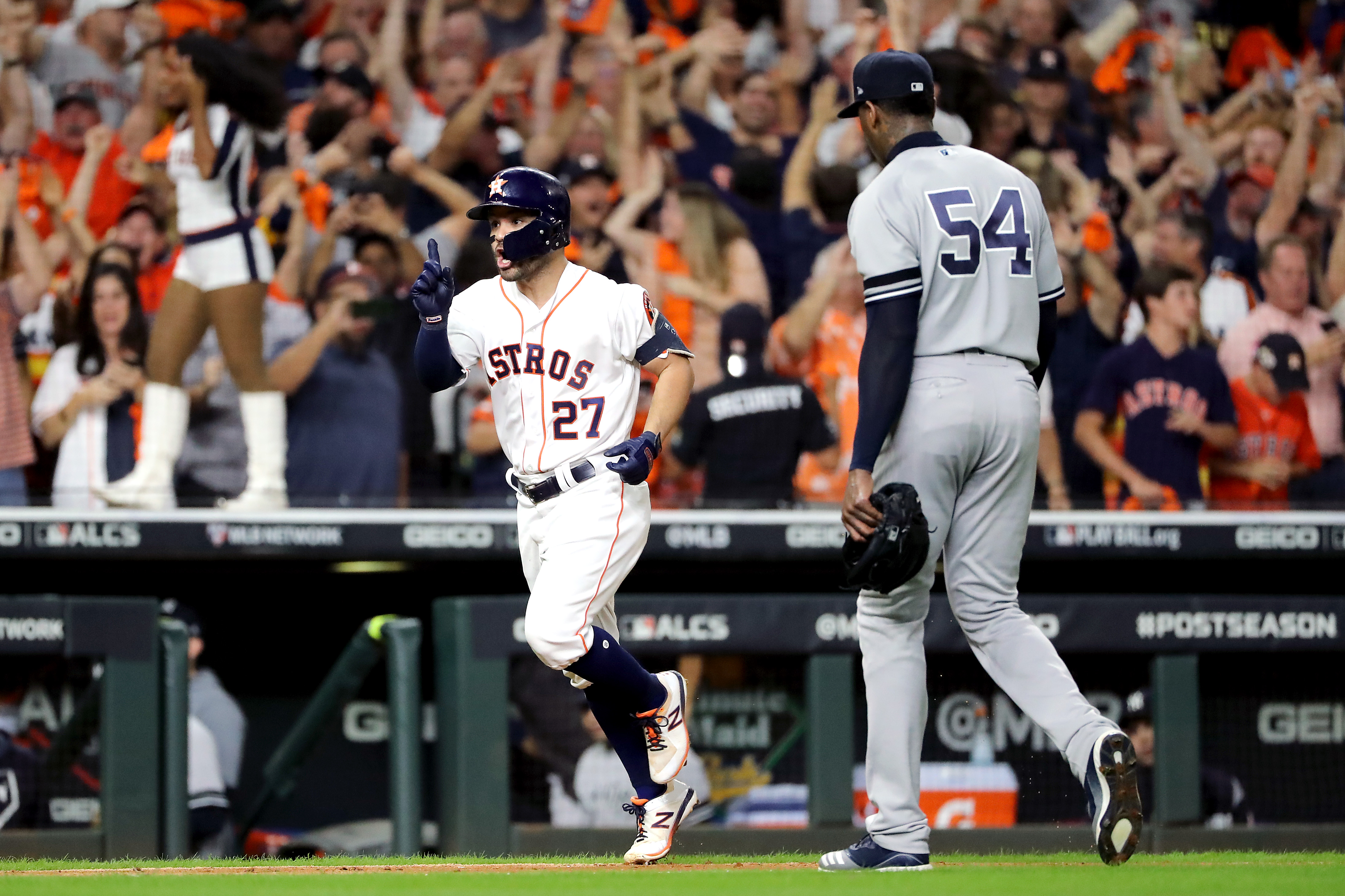 the Houston Astros’ Jose Altuve trots toward home plate past the New York Yankees’ Aroldis Chapman walking off the field as fans celebrate in the background