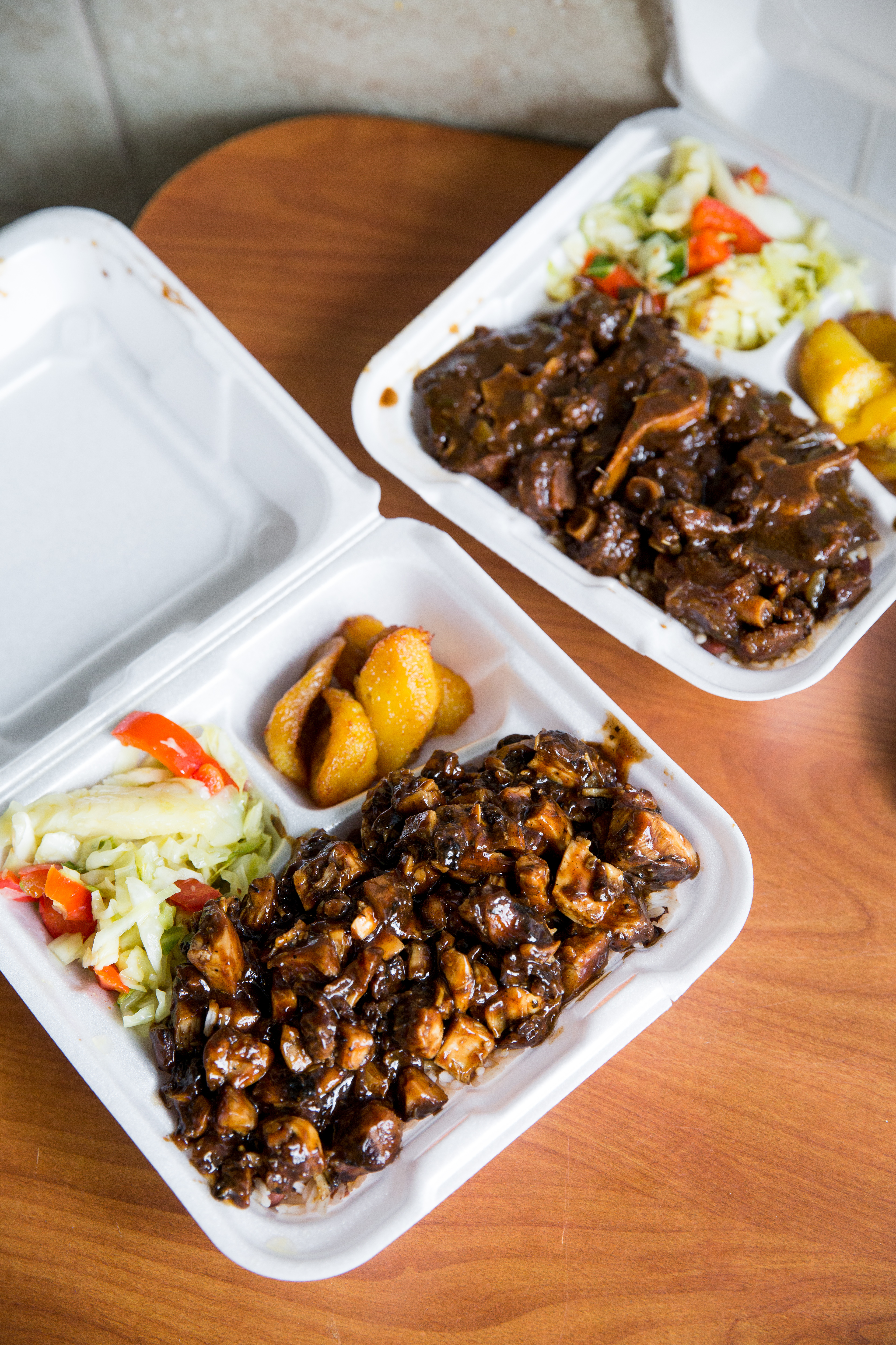 A carryout box filled with curried goat, salad, and plantains.