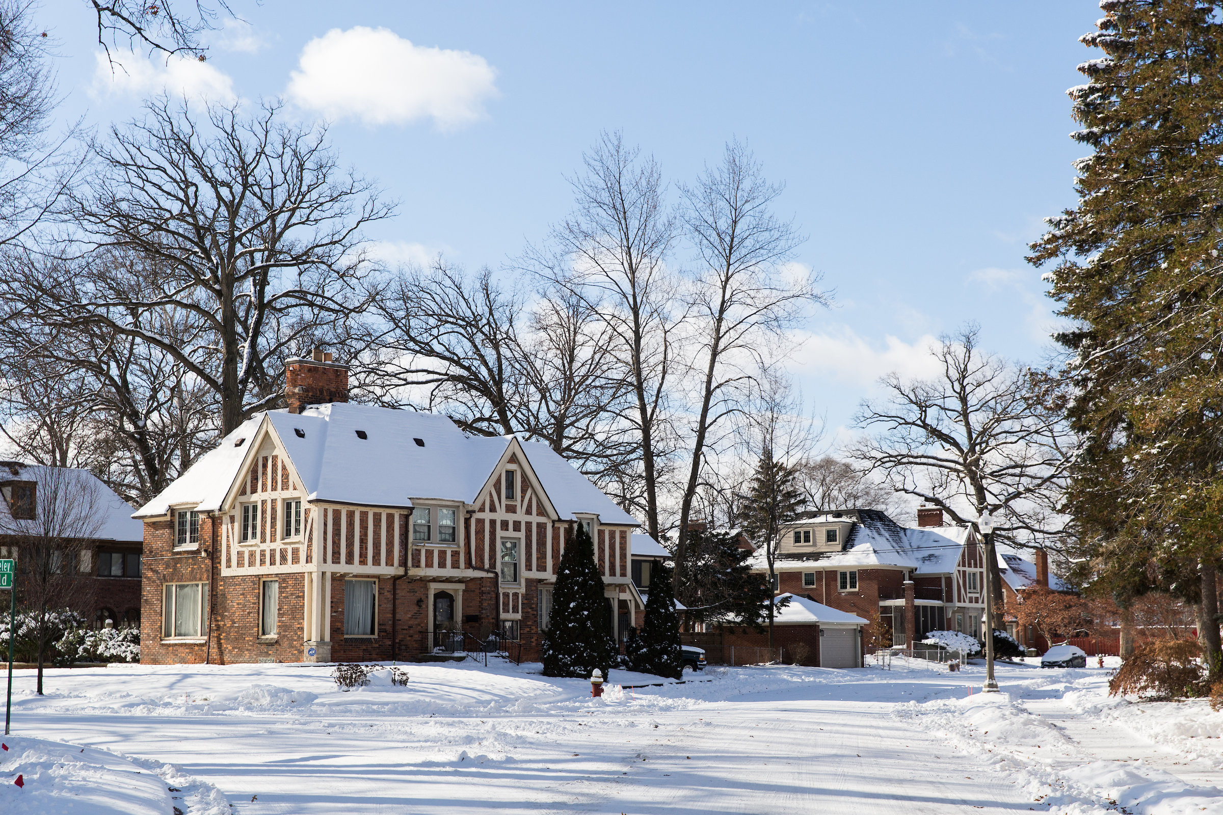 Two brown brick homes with roofs covered in snow. The road and sidewalks in the neighborhood are also covered in snow.