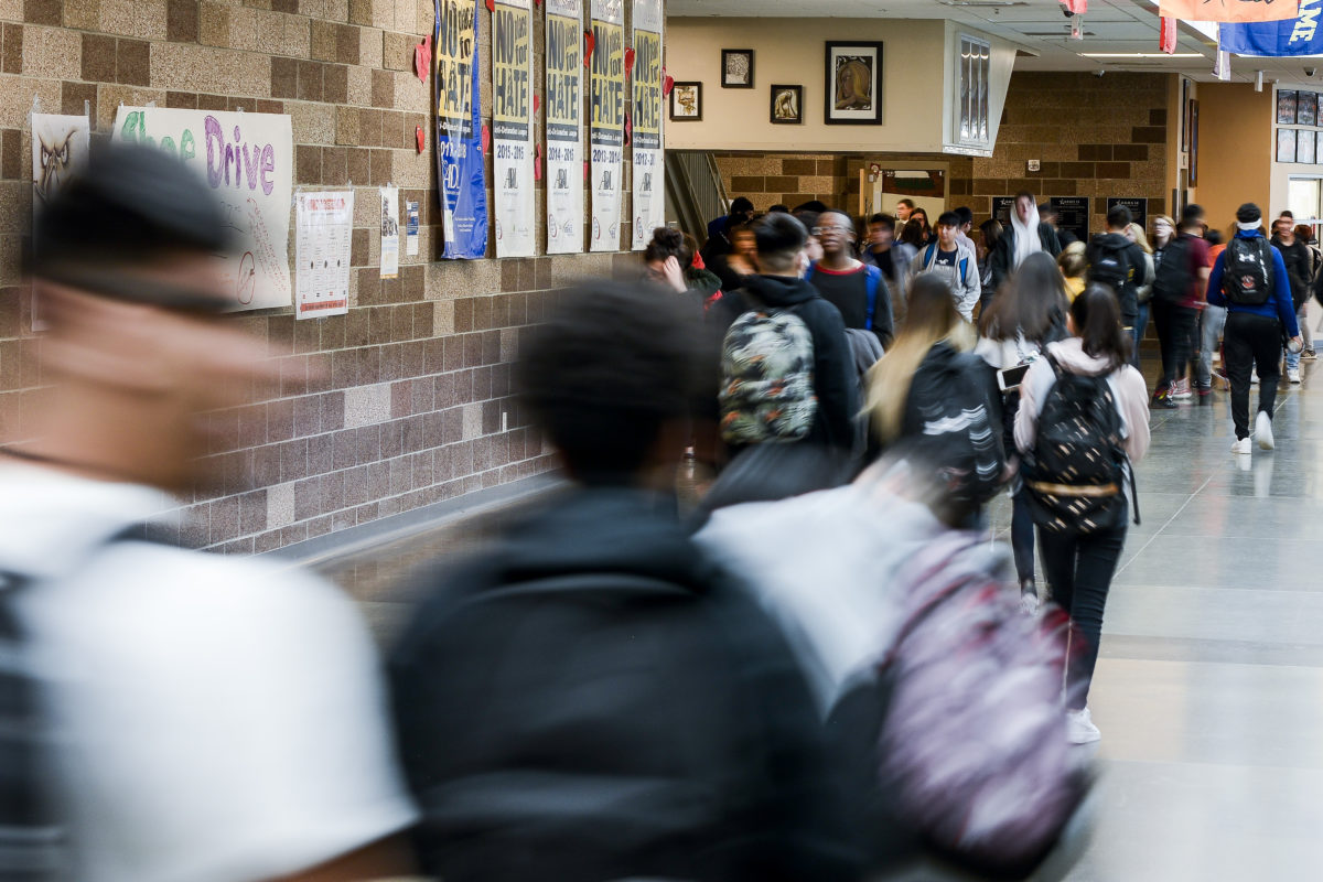 The backs of students as they walk through a hall at Adams City High School