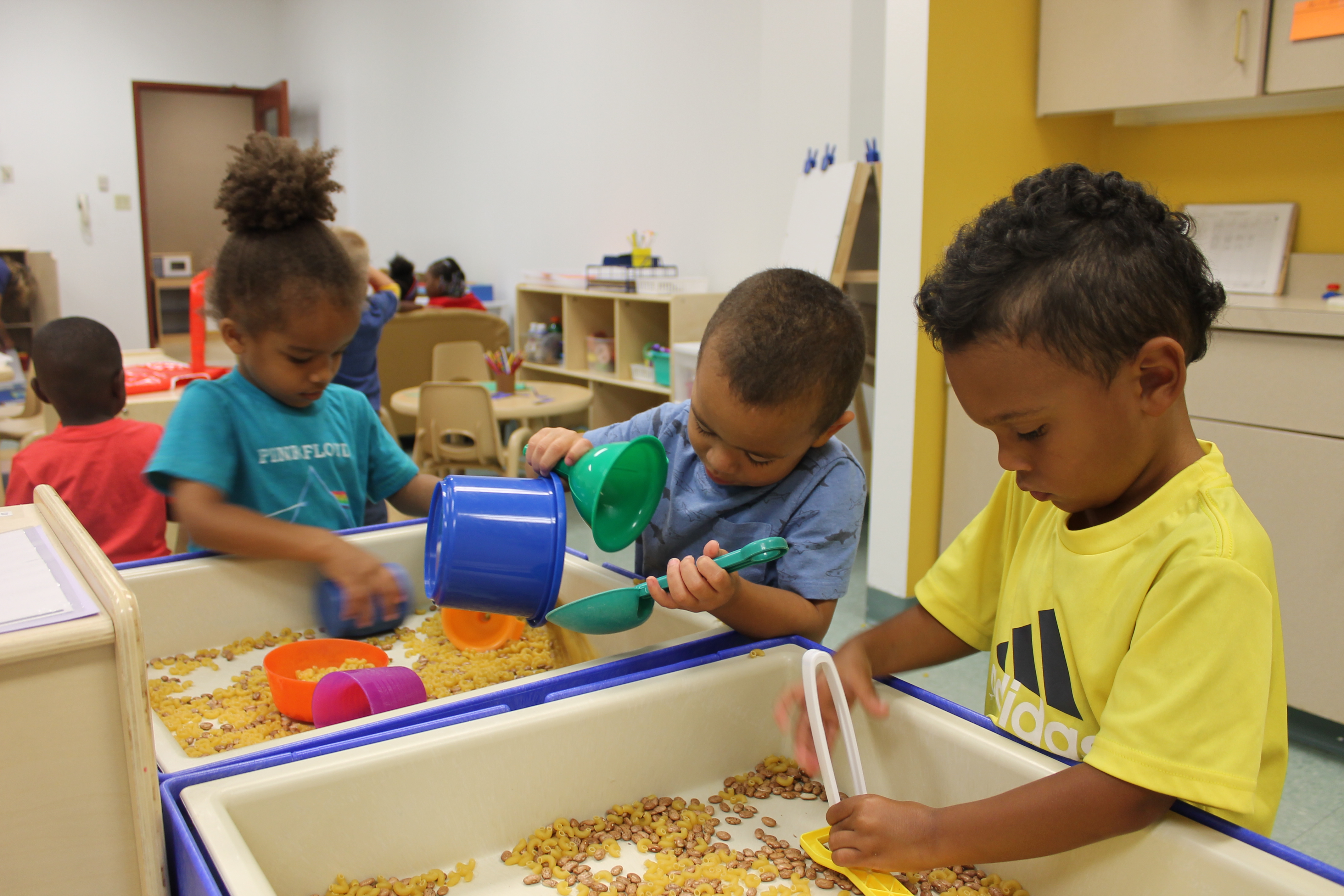 Preschool students play with beans and dried pasta at a sensory center in a preschool classroom at Day Early Learning at Eastern Star Church.