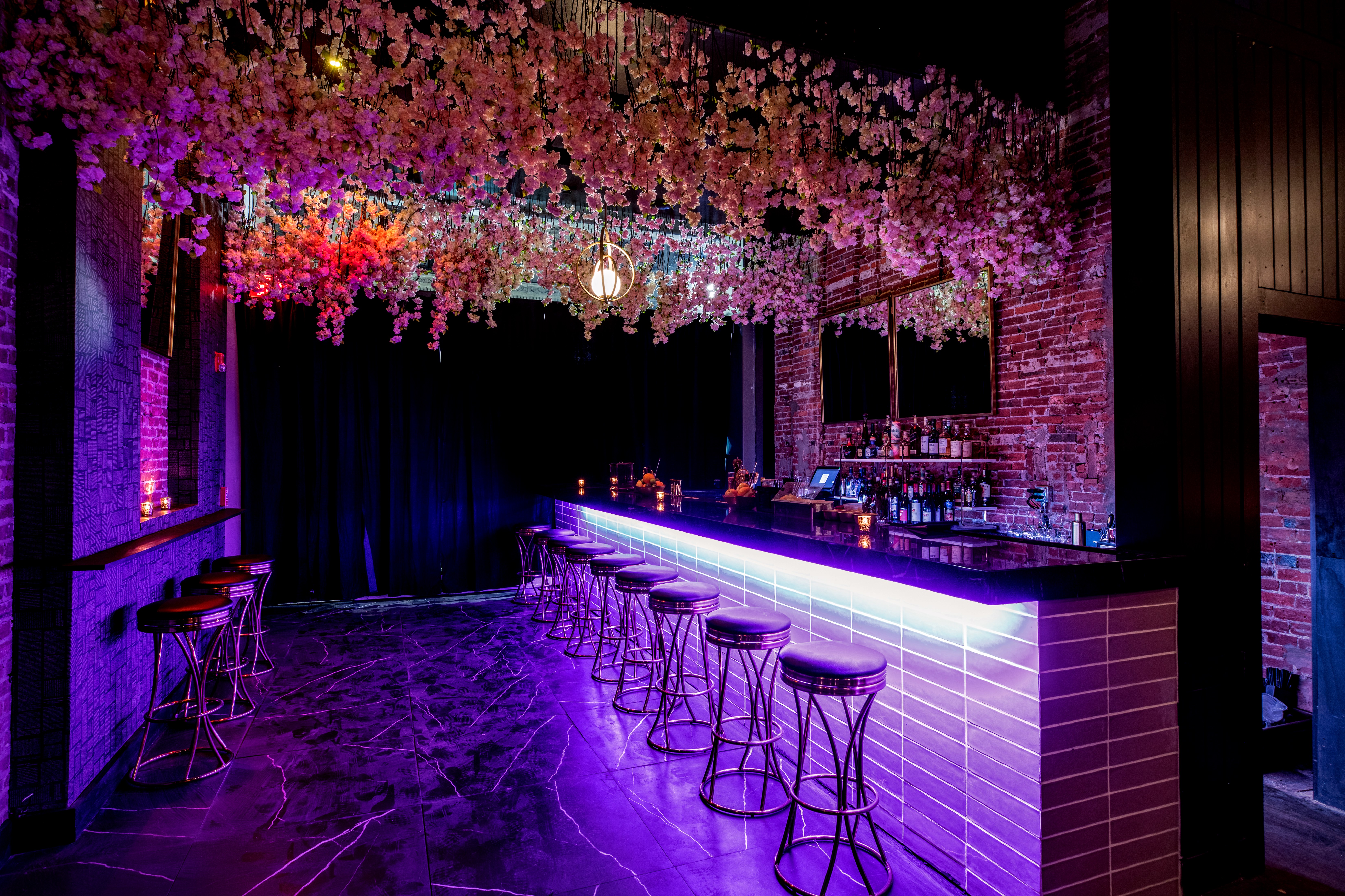 dark, purple-lit bar with flower curtain hanging above