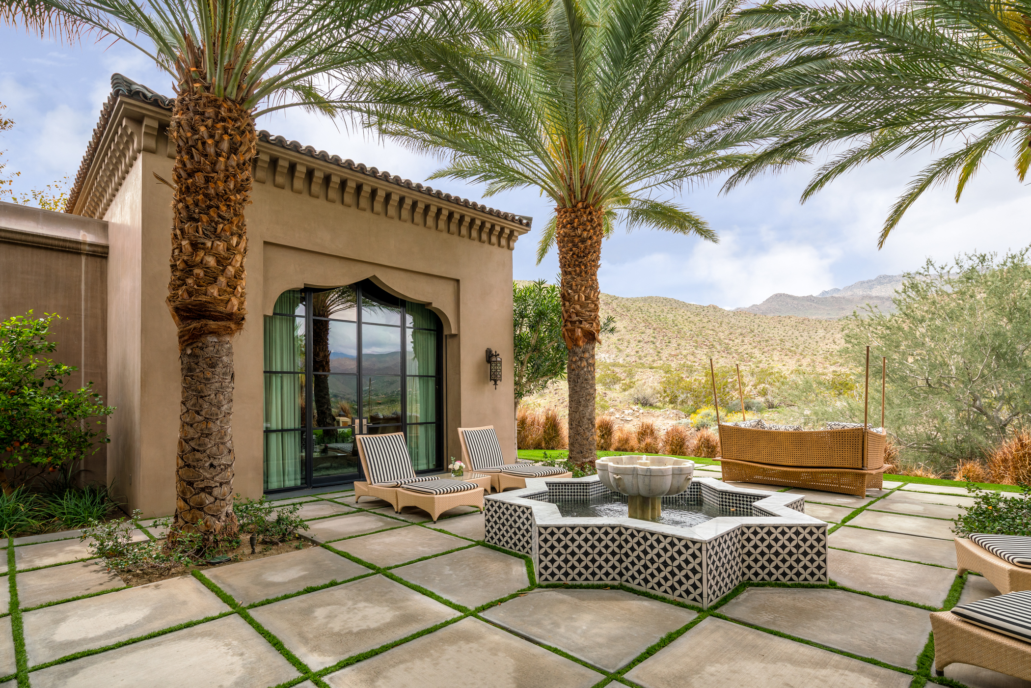 A Moroccan-inspired star fountain sits on a patio next to a boxy house in the desert. 
