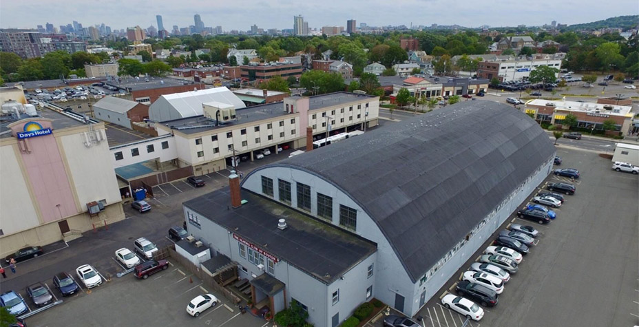 Aerial shot of a long building surrounded by parking, and the roof of the building is barrel-shaped.