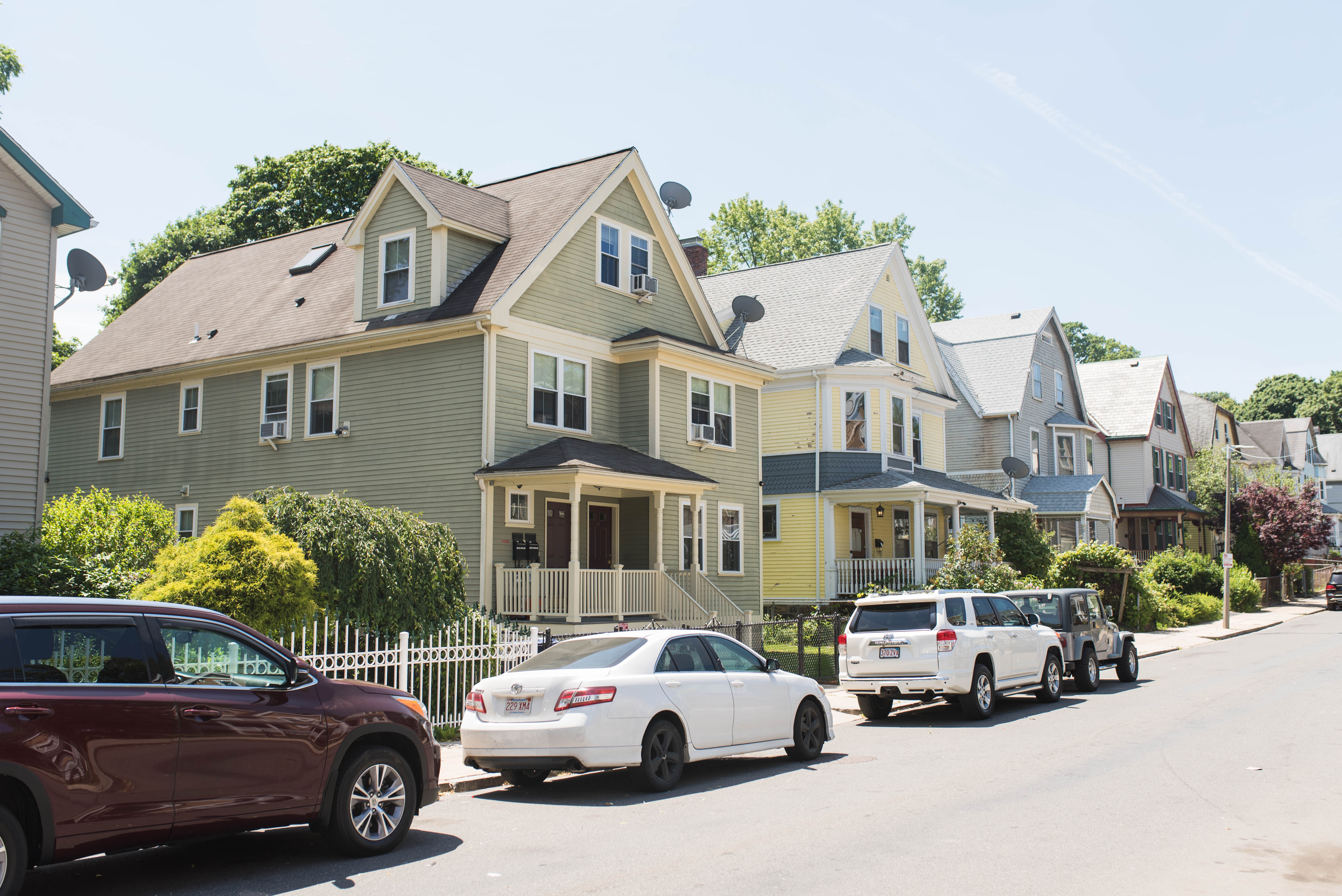 A row of two- and three-story houses along a city street with cars parked in front.