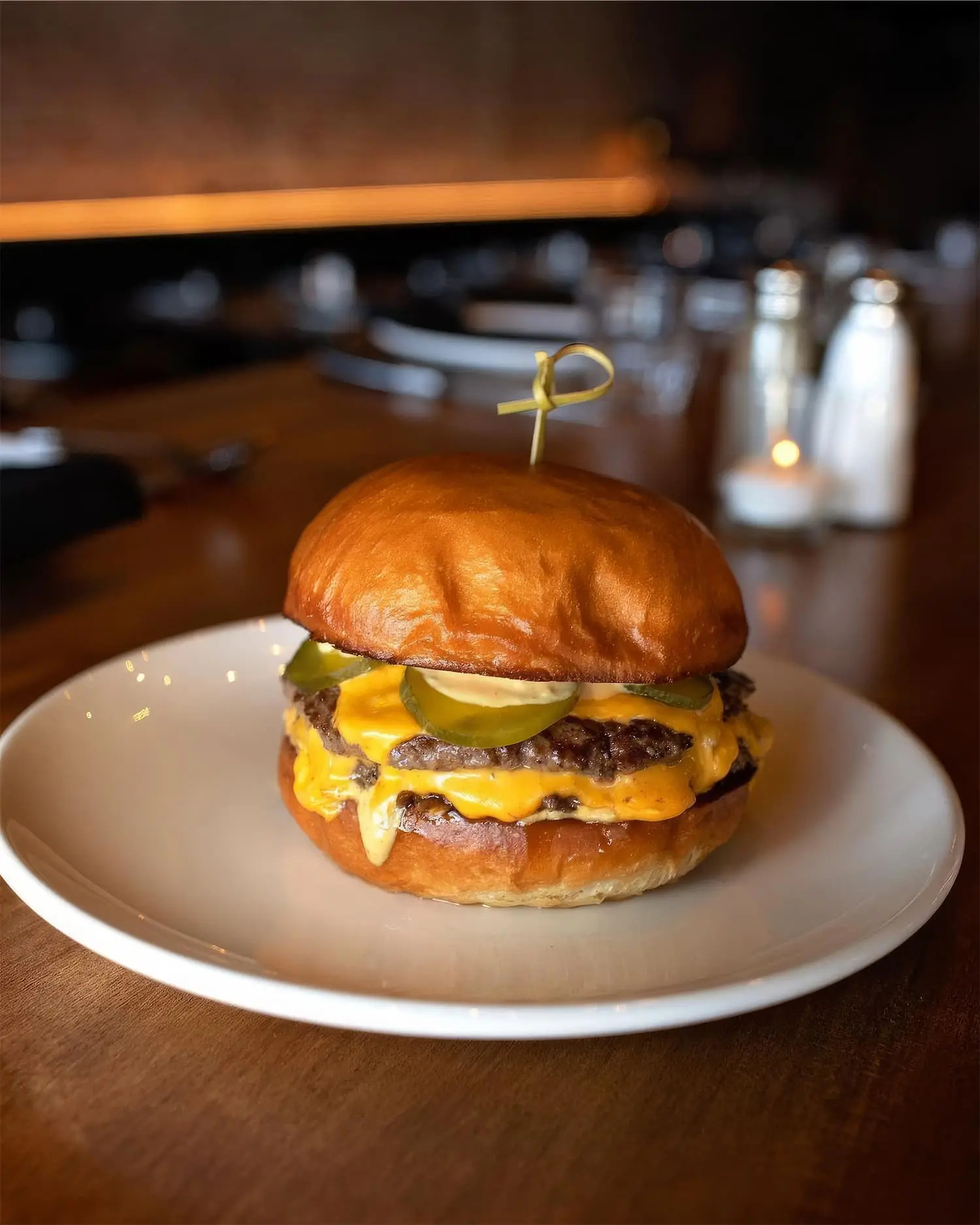 A burger with pickles and American cheese on a brioche bun.