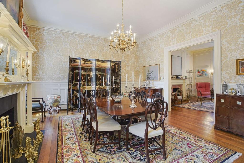 An ornate dining room with a table and chairs and a large opening leading to a living room.