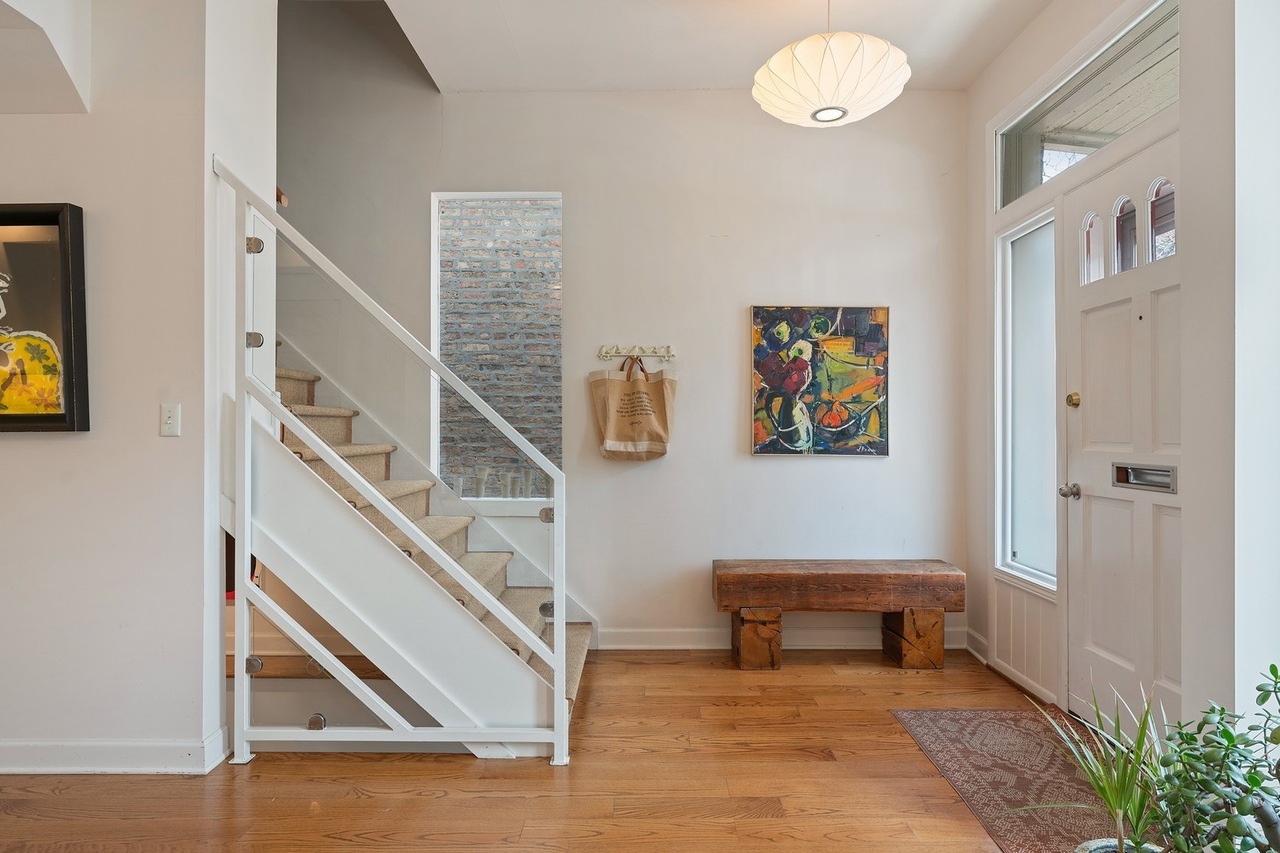 An entryway with a staircase, a painting, a paper light, and hardwood floors.