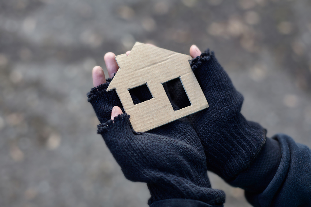 A pair of hands holding a cardboard cutout of a house.