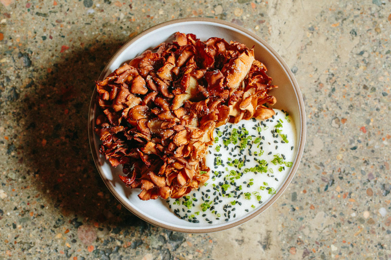 Overhead view of a round bowl full of a bloom of deep-fried hen-of-the-woods mushrooms and a white, herb-filled, foamy sauce