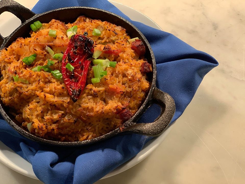 Yellow rice fills a cast iron pan, garnished with green onions and a grilled chile pepper. The pan sits on a blue cloth napkin.