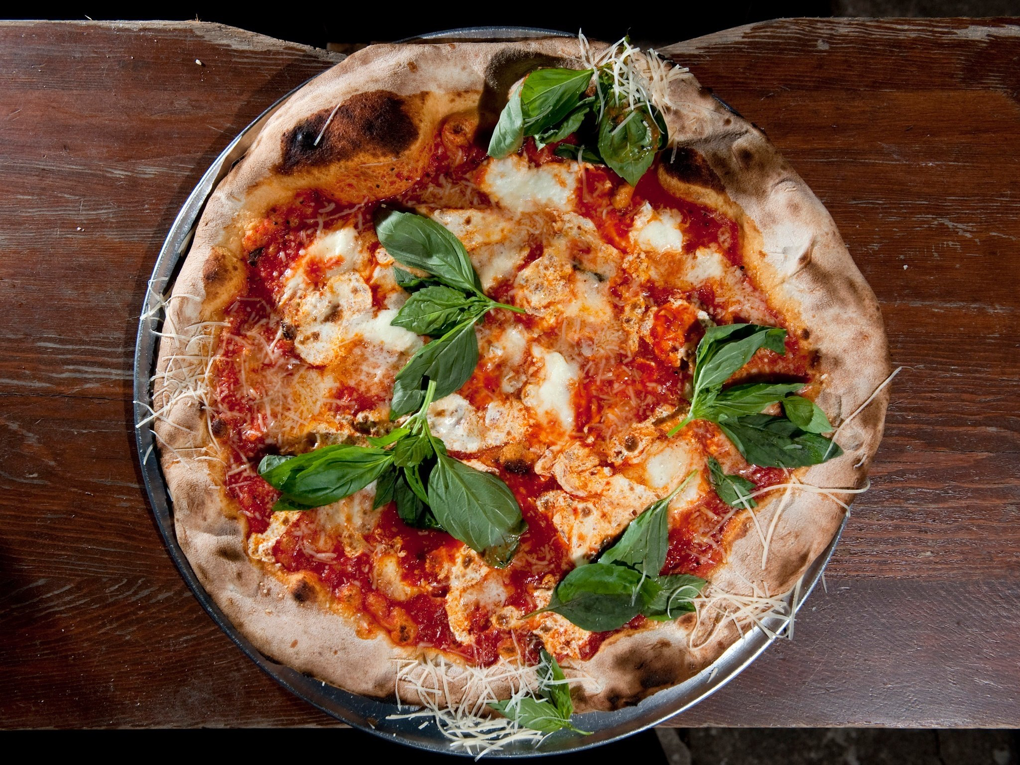 A thin-crust NYC-style pizza shown from above with red sauce and basil.