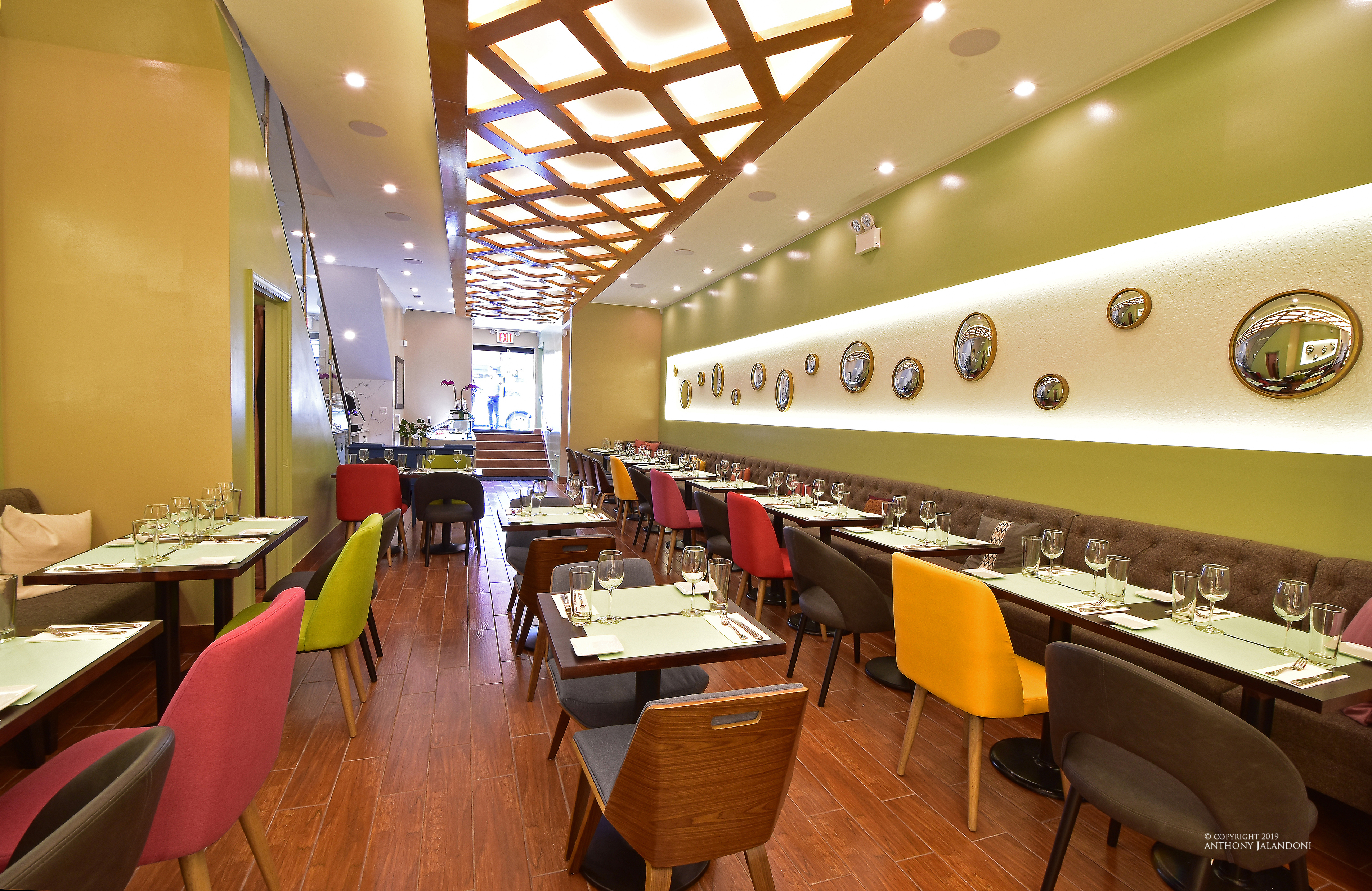 The green interior of a restaurant with colorful chairs and round mirrors on the walls