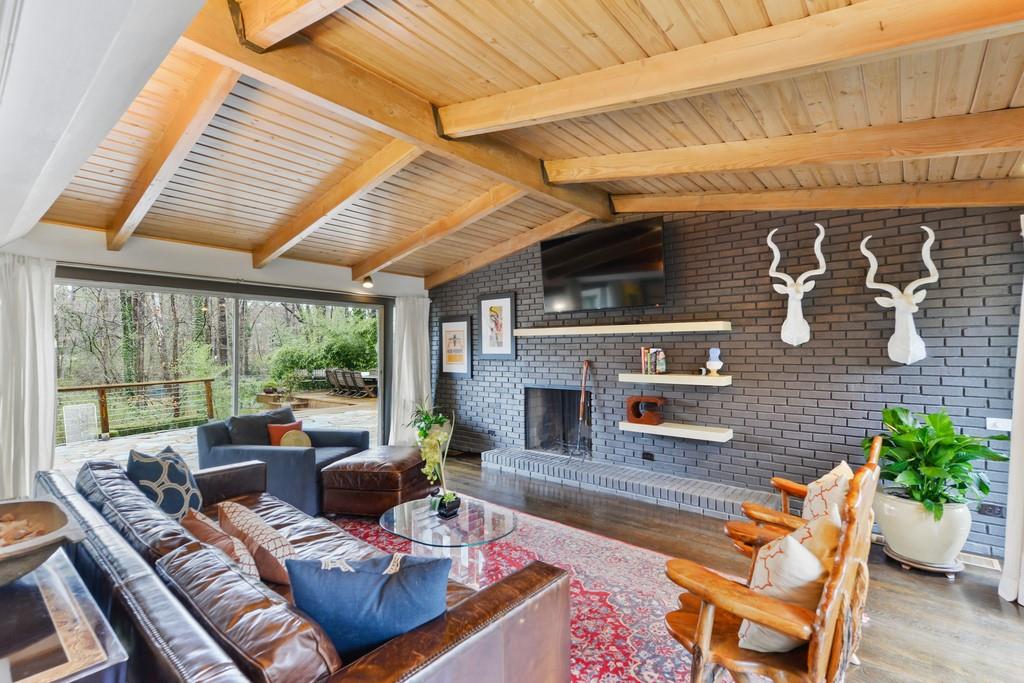A midcentury modern living room with a fireplace and tongue-and-groove wooden ceiling with leather furniture.